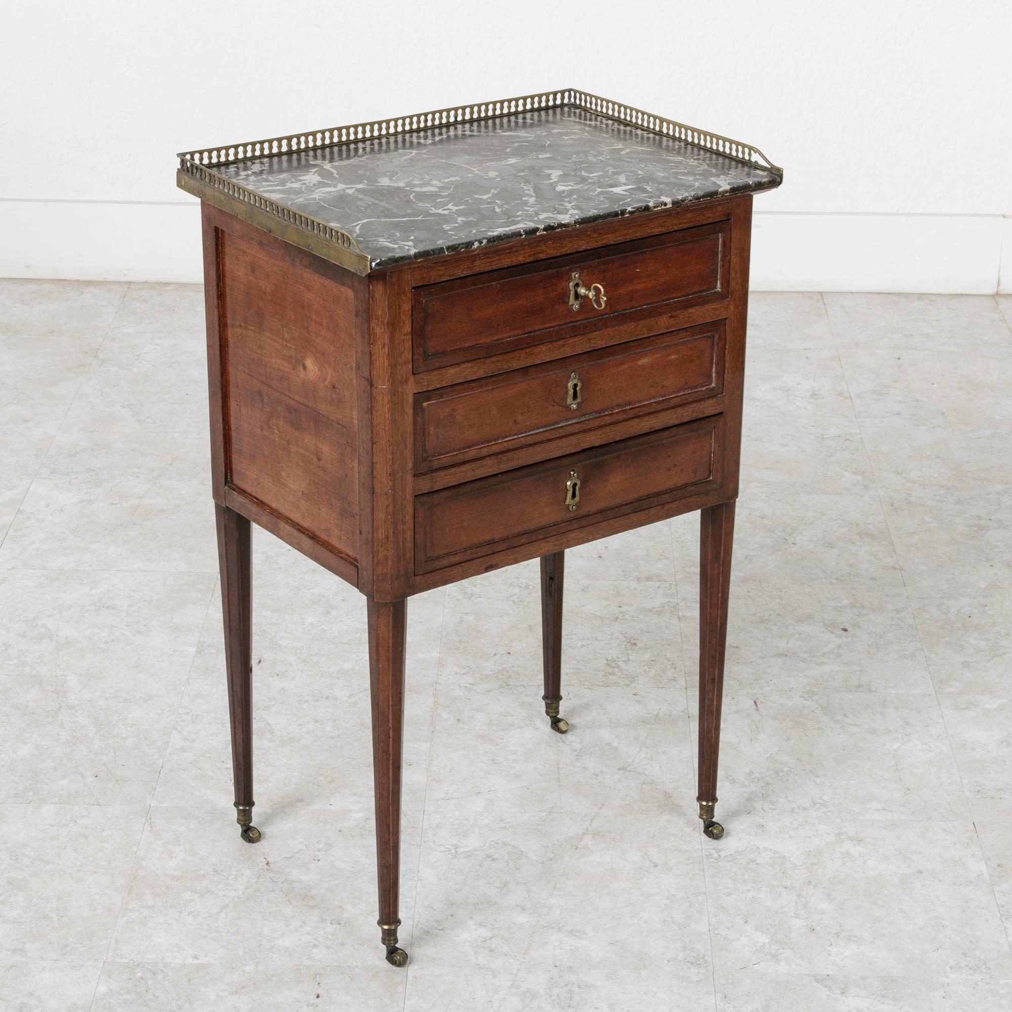 Found in Deauville, France, this small-scale, 18th century mahogany nightstand or side table features a Saint Anne marble top surrounded by a bronze gallery. Its octagonal, tapered legs rise on bronze casters. With three hand hewn, dovetailed
