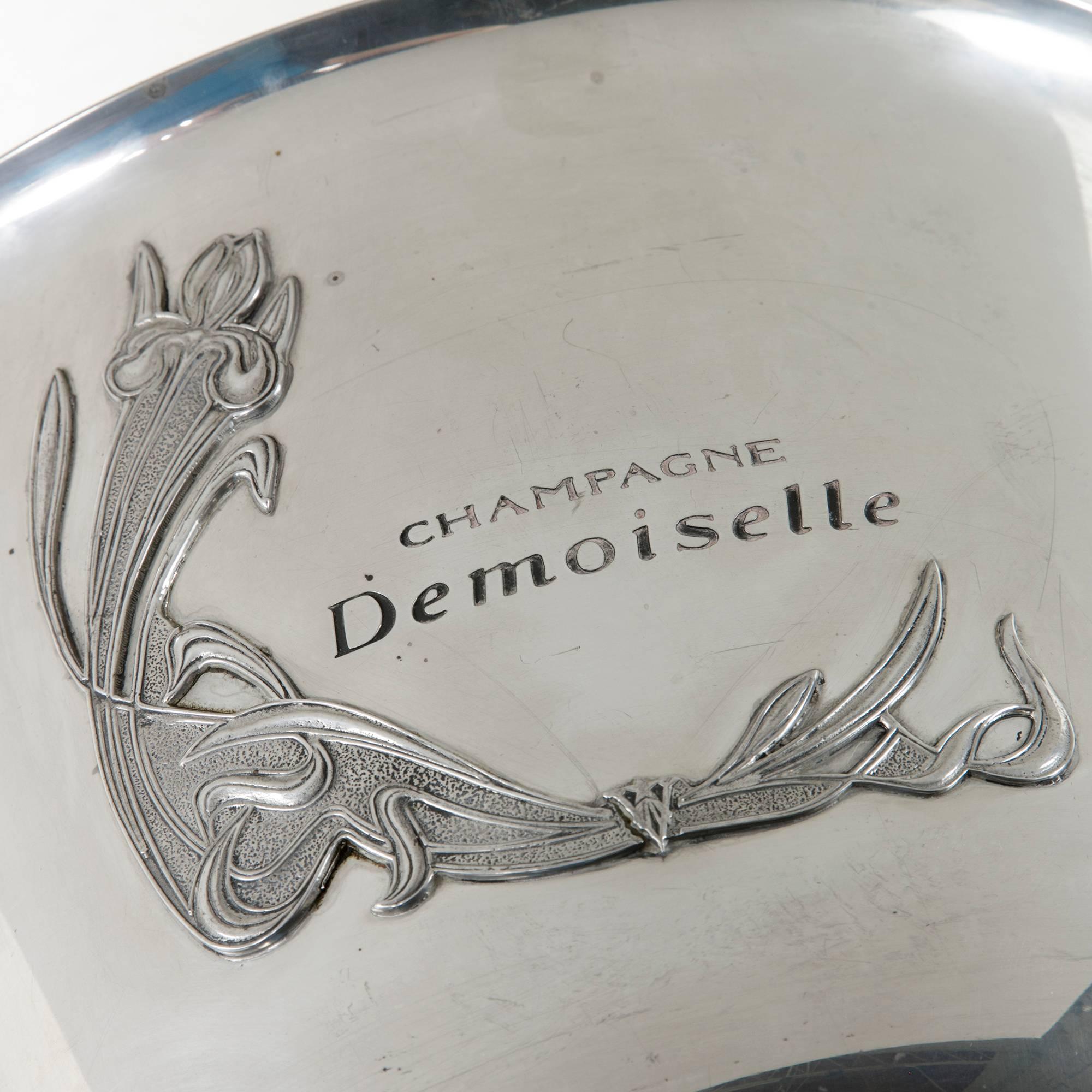 This 20th century silver plate champagne bucket was originally used for hotel service. Bearing the mark of the champagne demoiselle and its art Nouveau motif, this wine chiller holds six bottles. The Demoiselle champagne is named for the vineyards