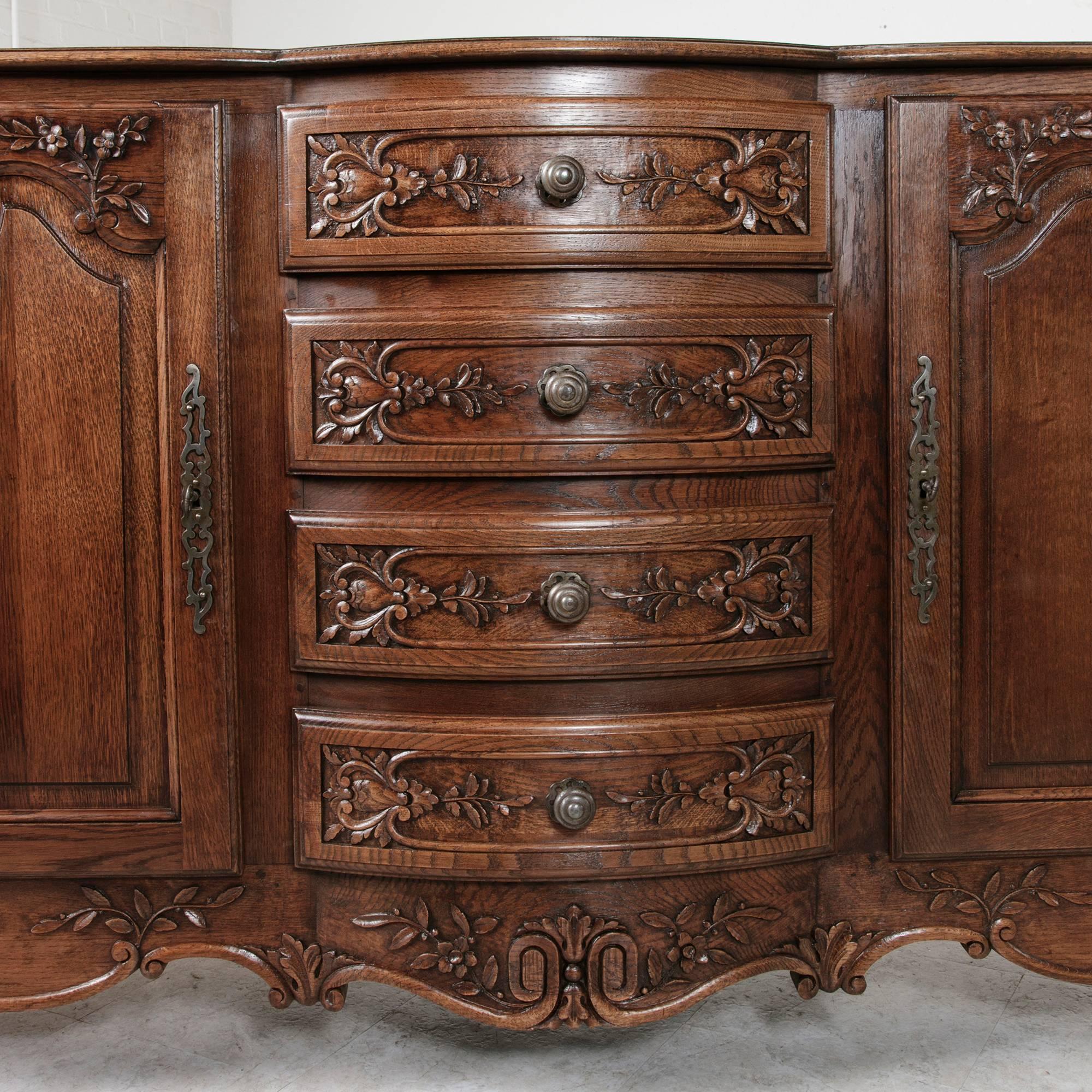 This hand-carved oak Louis XV style enfilade with bombe front boasts four center drawers, creating ample storage for your dining space. The side doors feature symmetrical acanthus leaf carvings and conceal two single interior shelves. A curved top