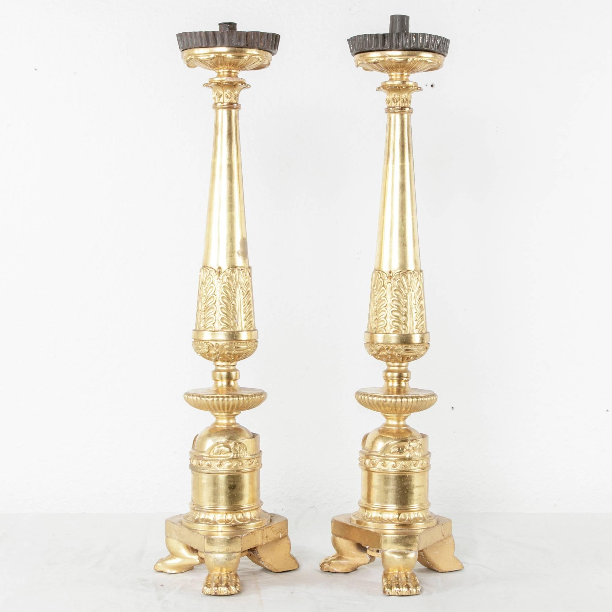 This pair of giltwood French Empire period prickets or candlesticks was originally used on the altar of a church. They were hand-carved and exquisitely gilded on only one side as a means of economy for the Church. Two of the three legs feature