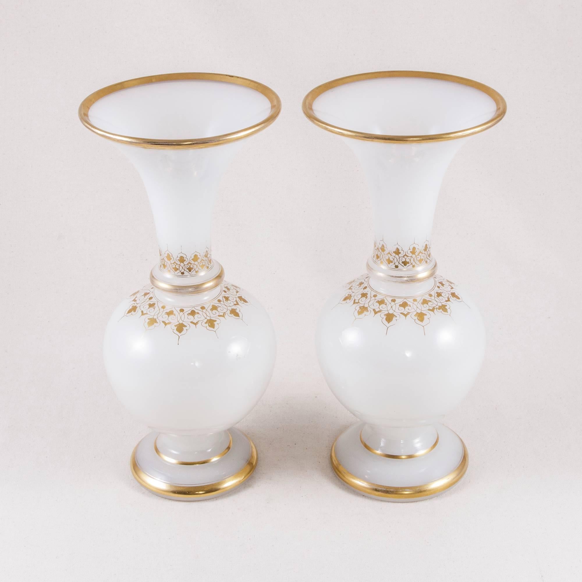 This turn of the century pair of French opaline vases with hand-painted gilding features a delicate pattern of intertwining grape leaves and vines. Accents of hand-painted gold bands around the upper rim are mirrored at the base, adding to the regal