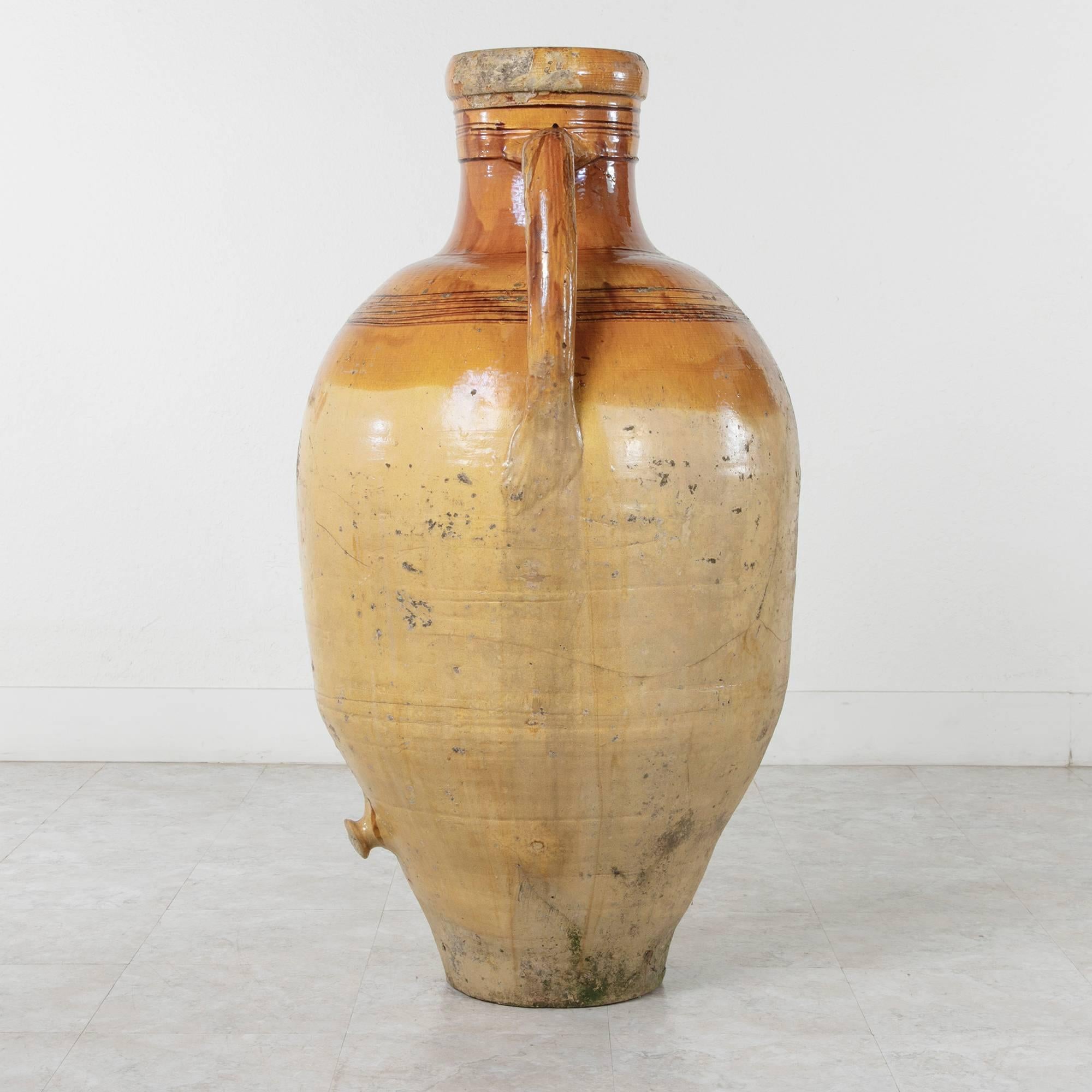 This circa 1900 large yellow faience olive oil jar hails from Naples, Italy. The double handles and lower spout of this Amphora reveal a beautiful patina from the handling of the olive oil once stored inside. A wonderful Mediterranean addition to