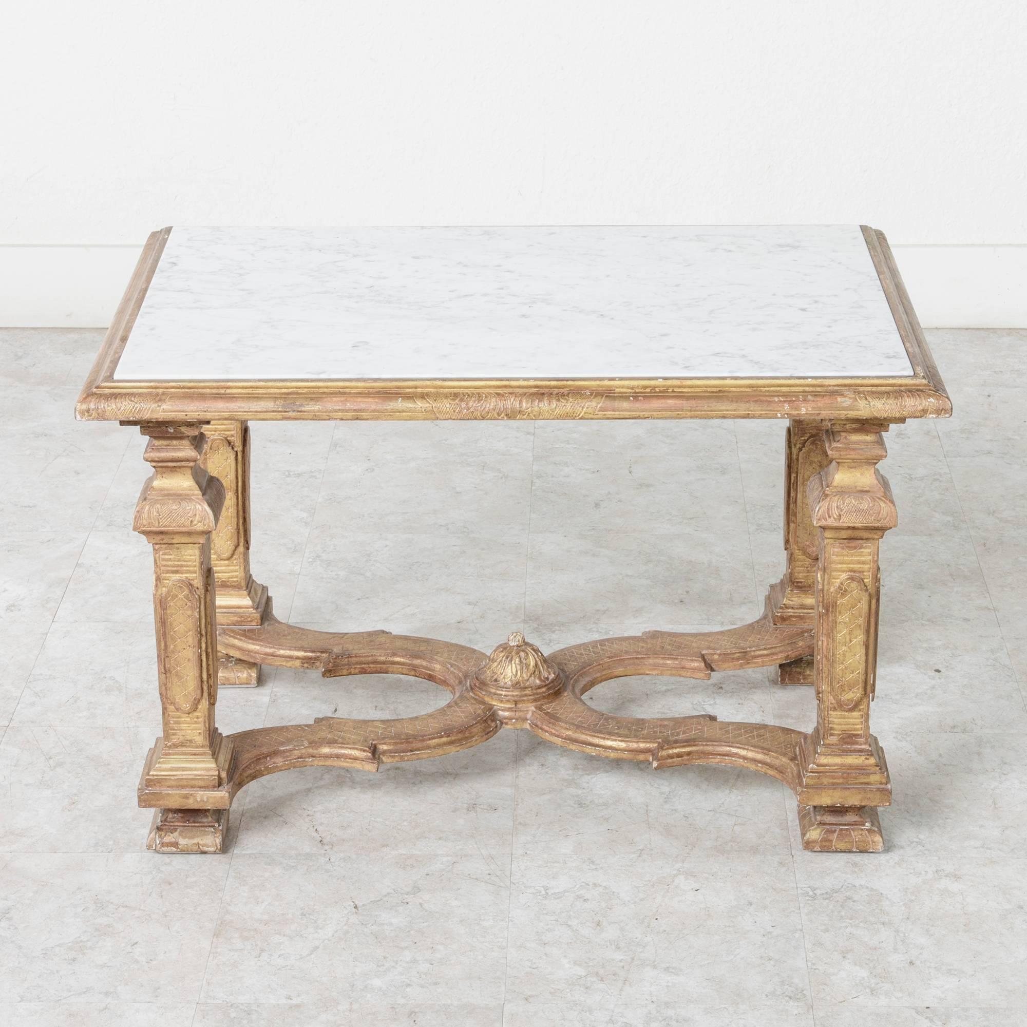 This Mid-Century giltwood Italian cocktail or coffee table is presented in the Louis XIV style. It features square baluster legs with incised carvings and an X-stretcher culminating in a dome shaped finial draped with acanthus leaves. An inset of