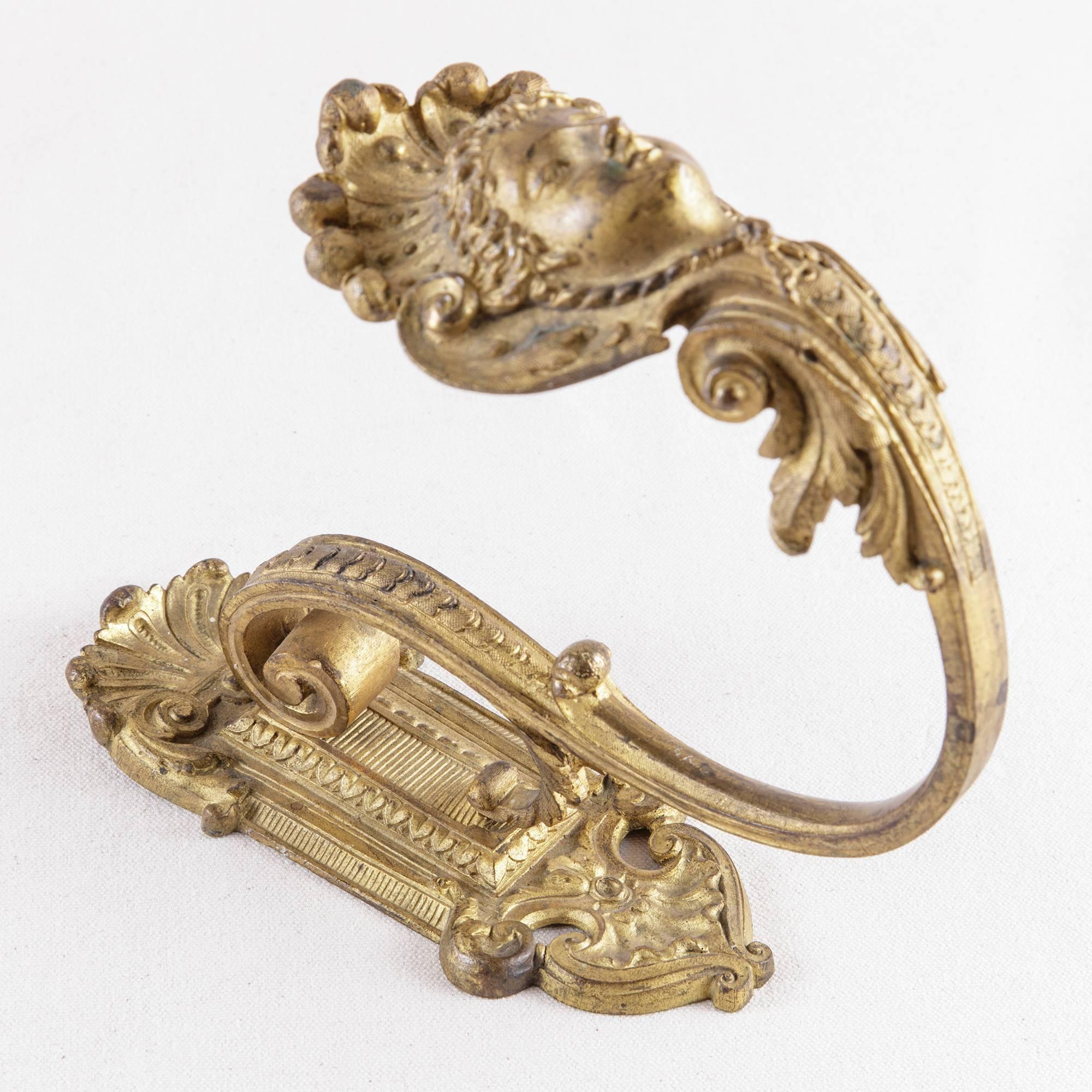 This large-scale gilt bronze hook from the 19th century features a Regency style female mask crowned with a palmettes. It originally hung on the wall as a drapery hook in a French salon. Its large-scale makes it ideal as a towel hook in a bathroom.