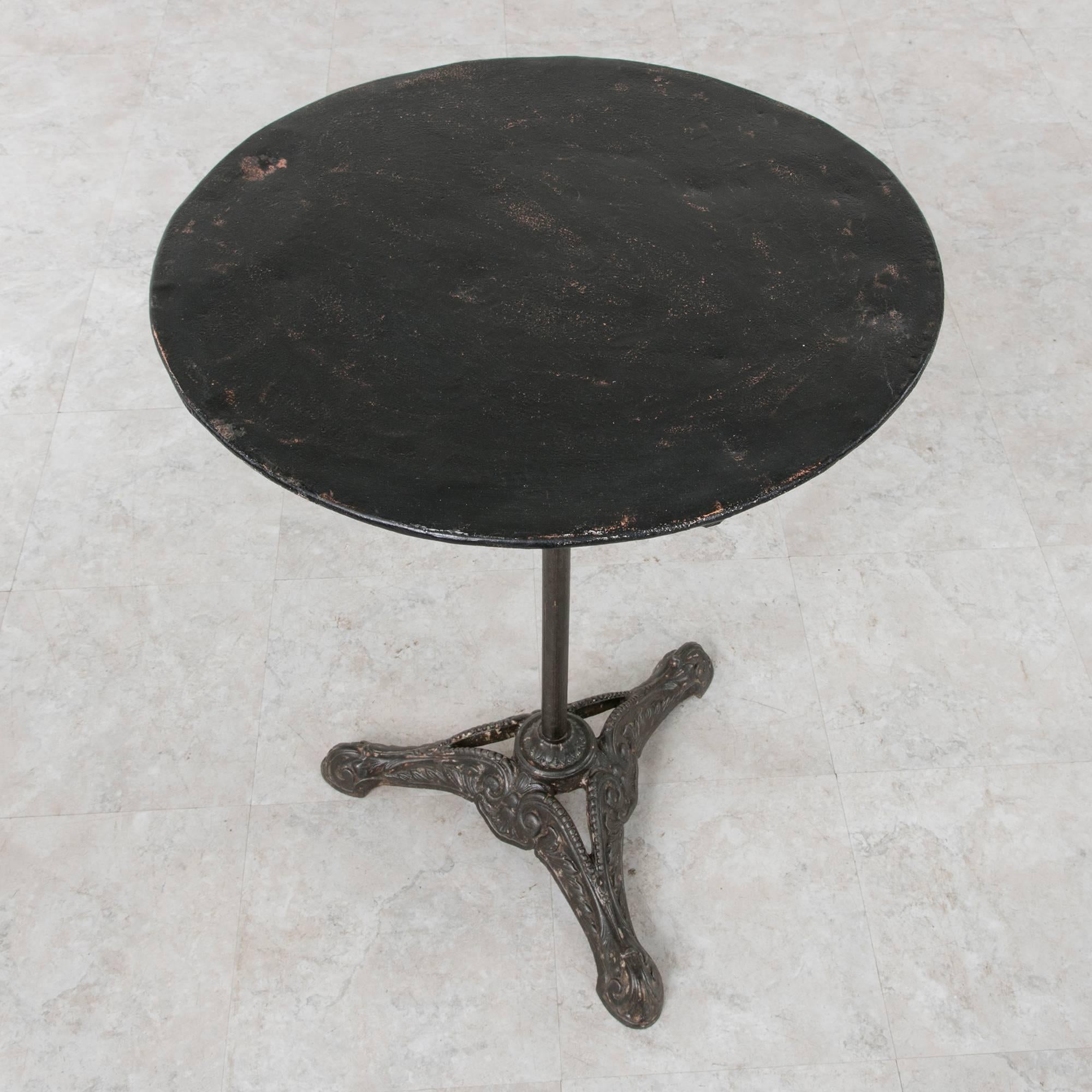 This iron bistro table from the turn of century boasts a Classic design that has stood the test of time in outdoor French cafes. Its heavy cast iron tripod base features escargot feet that transform into acanthus leaves with beaded accents. The