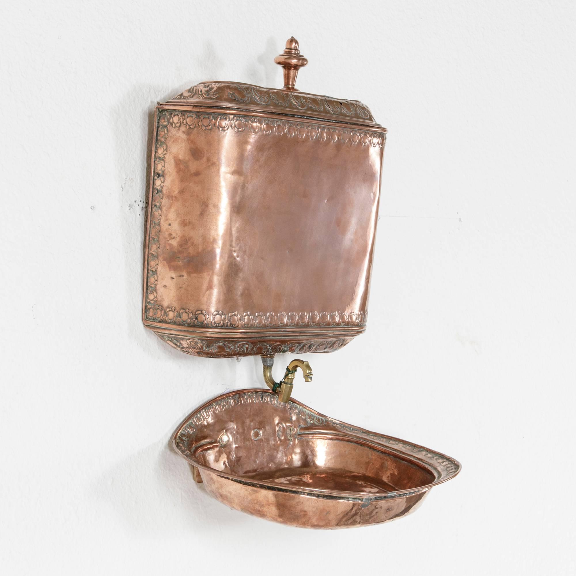 This 18th century copper repousse fountain was originally mounted on the wall inside the home. This Louis XVI period piece features intricately hand-hammered repousse work on the basin, fountain and lid and its original bronze handle and spigot.