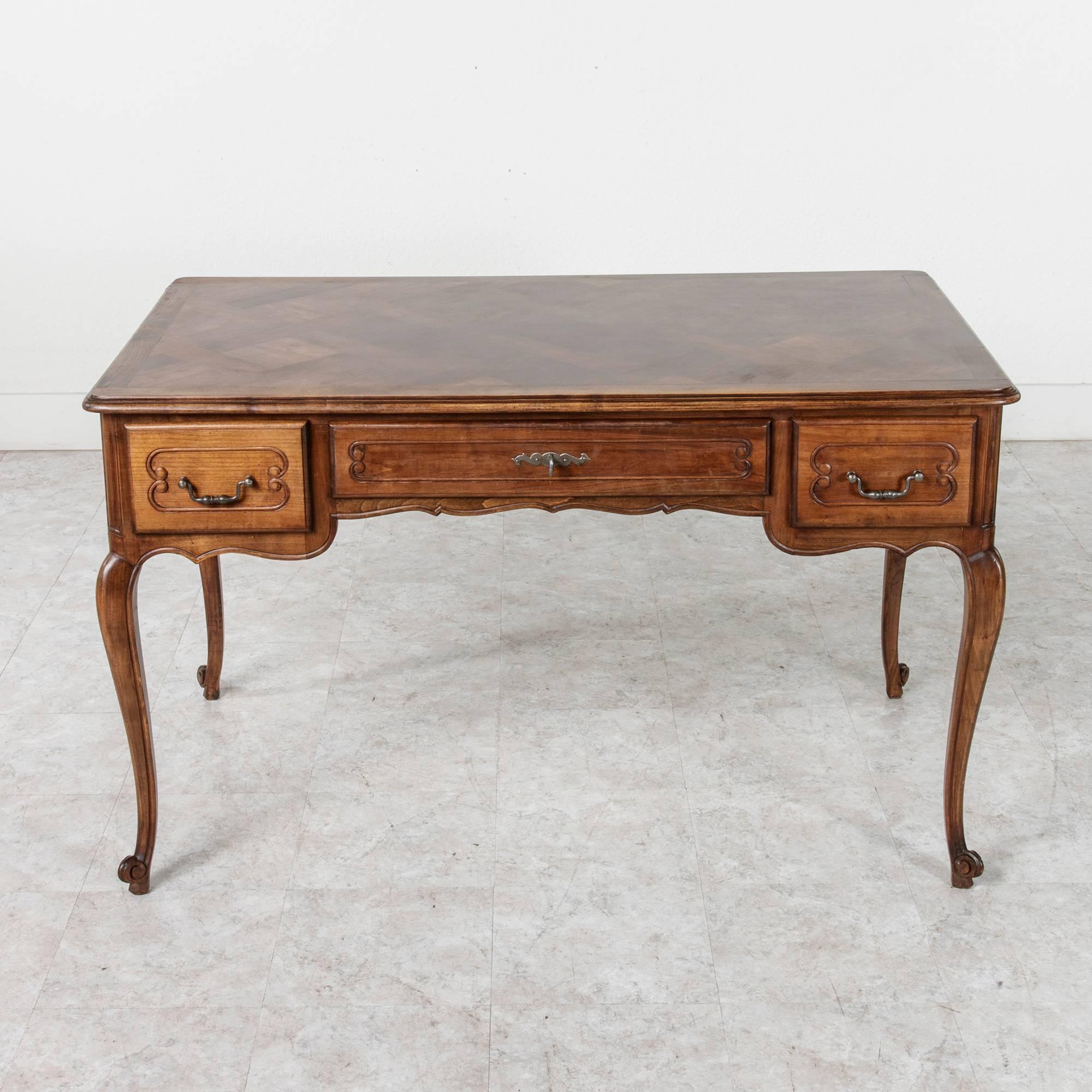 This elegant walnut Louis XV style desk features a parquet top and three drawers. Double faced with carved recessed panels on all sides, it stands on tapered cabriole legs that lead to Classic escargot feet. This elegant desk marries form and