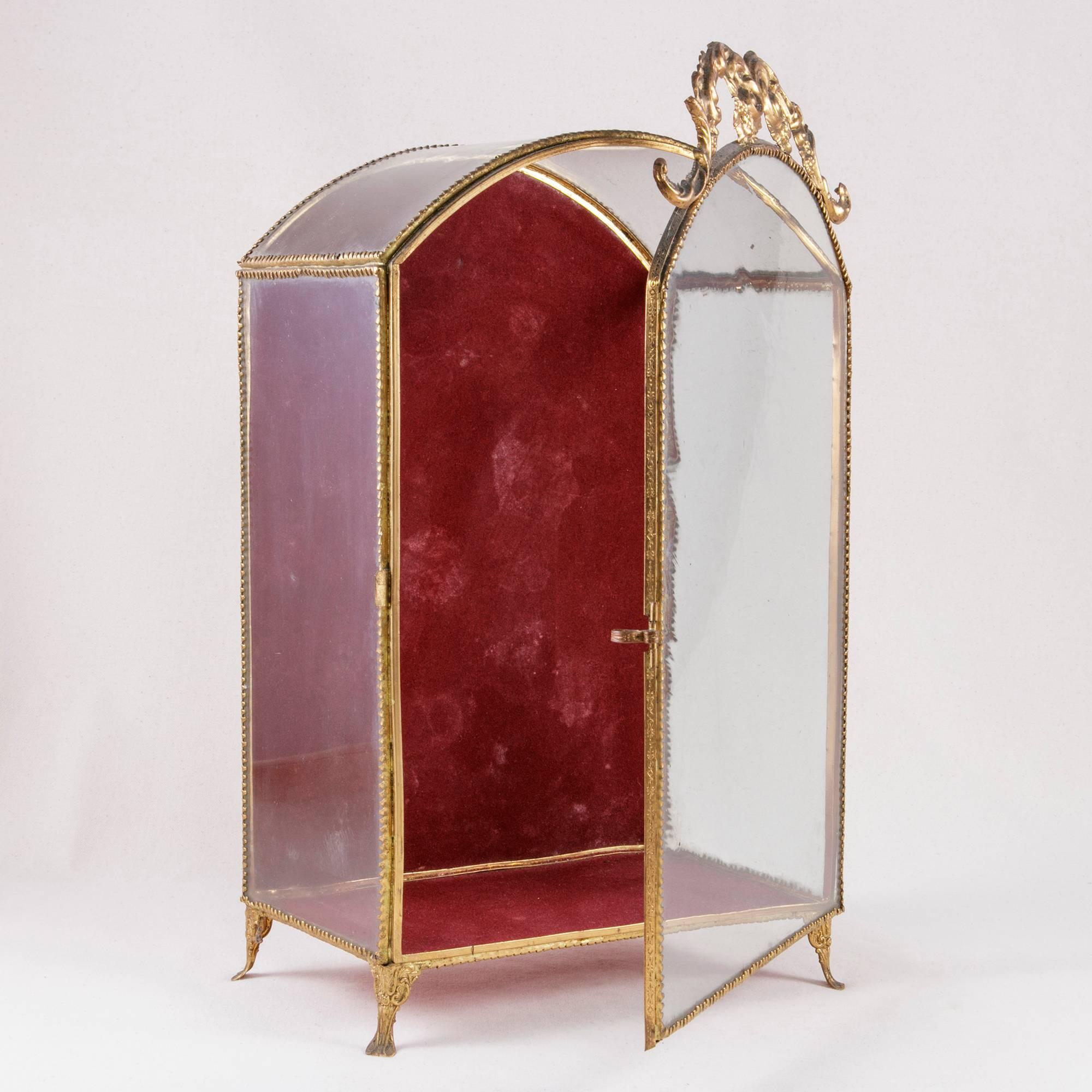 This late 19th century brass tabletop vitrine was originally used to display the floral garland headpiece worn by a French bride. It stands on detailed brass feet and features brass ormolu banding surrounding its original glass panes. The bonnet top