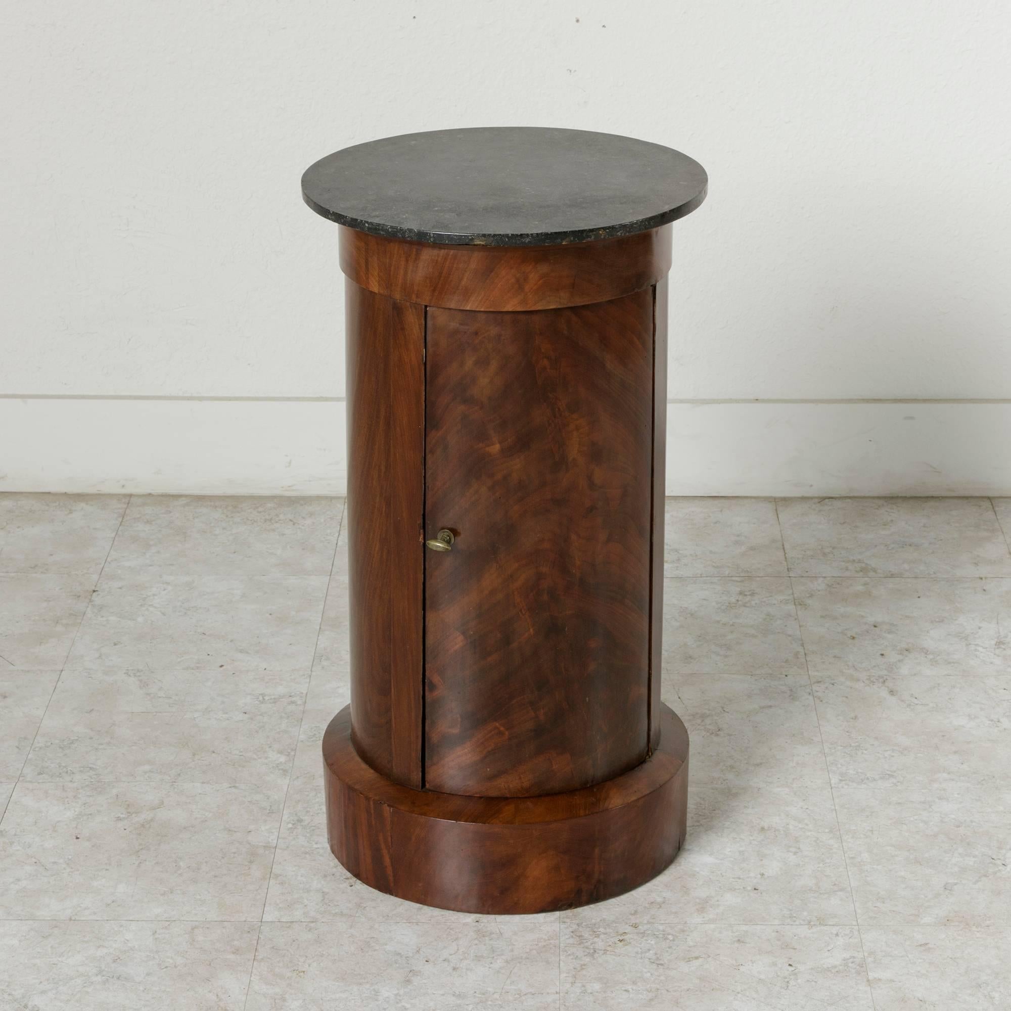 This stunning French Empire period mahogany somneau or drum table features a black marble top and hinged curved door. Its cylindrical form and clean lines lend a refined yet modern character. Its interior includes a marble shelf and provides the