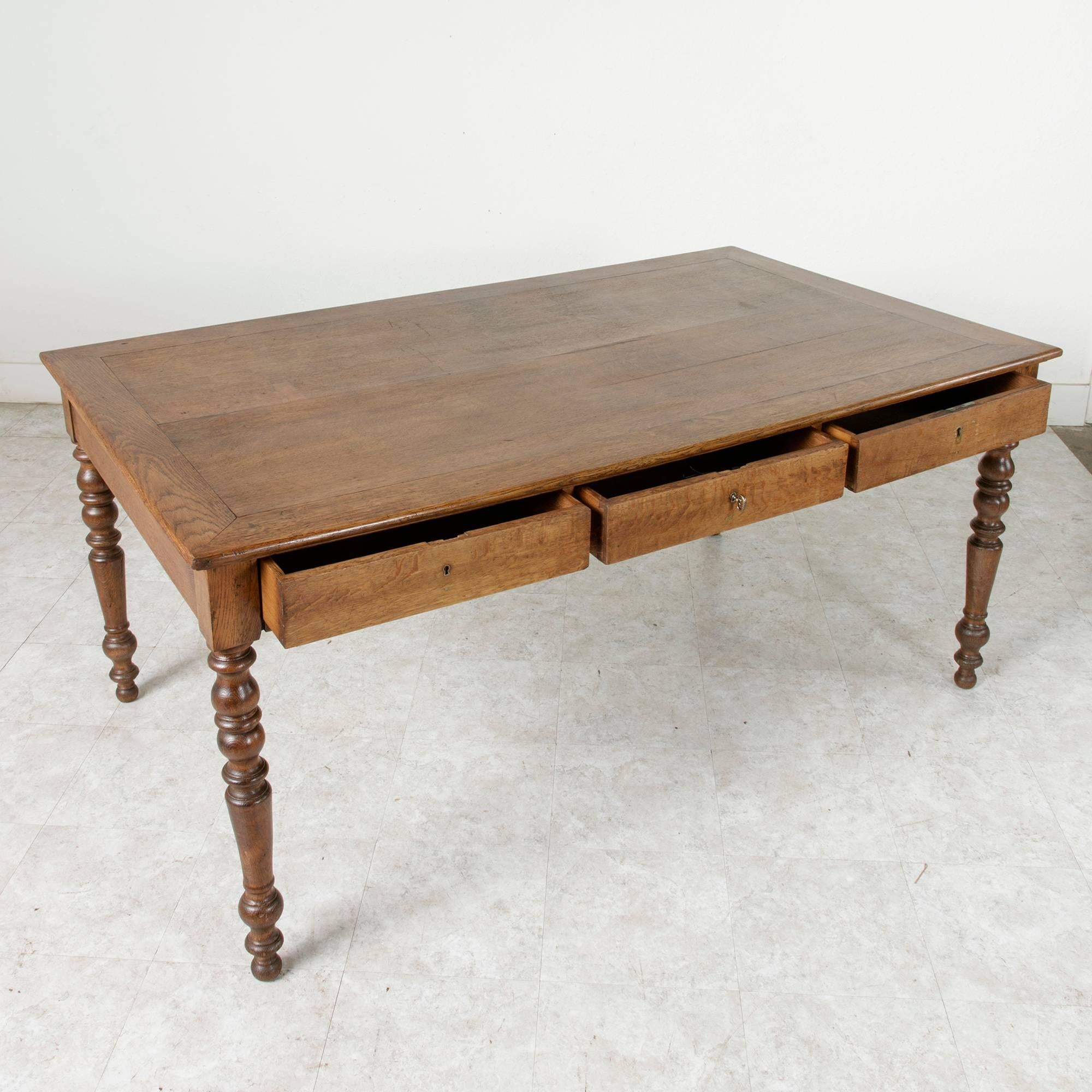 This turn of the century artisan-made oak farm table features hand-turned legs and three drawers on one side, ideal for storing place settings, silverware, or table linens. With its simplicity in form and age-worn wood, this circa 1900 Normandy farm