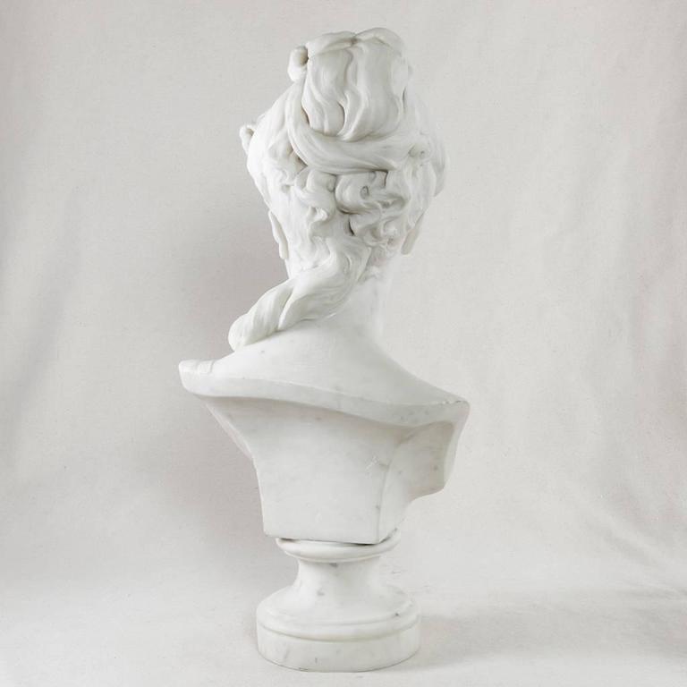 This late 19th century beauty in marble wears a crown of flowers and leaves in her elaborate coiffure. Resting on a short pedestal, this marble bust of a young woman is signed behind her left shoulder by the nineteenth century French sculptor Rene
