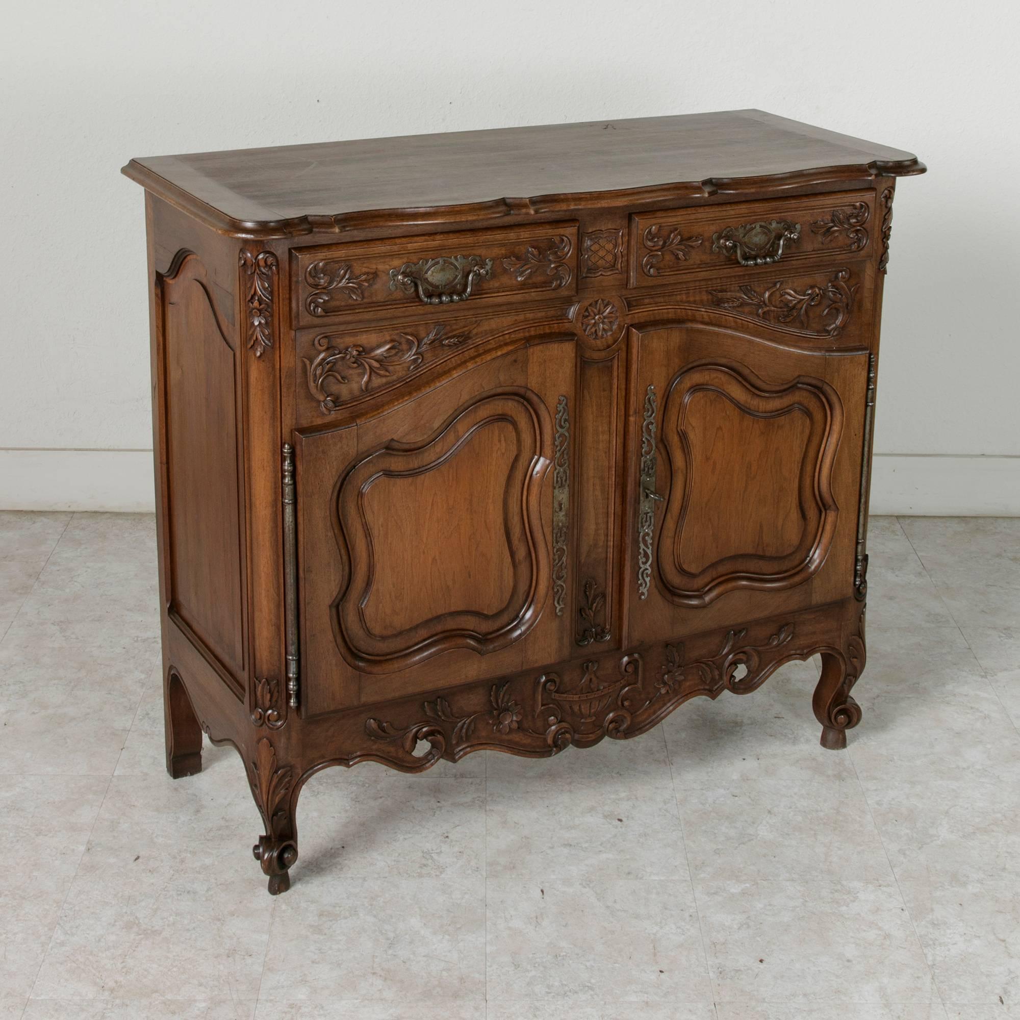 This beautiful Louis XV style walnut buffet from the early twentieth century features a wide array of carvings. Detailing includes carvings of leaves, wheat, flowers, a central rosette, and on the apron, the traditional soup tureen which is the