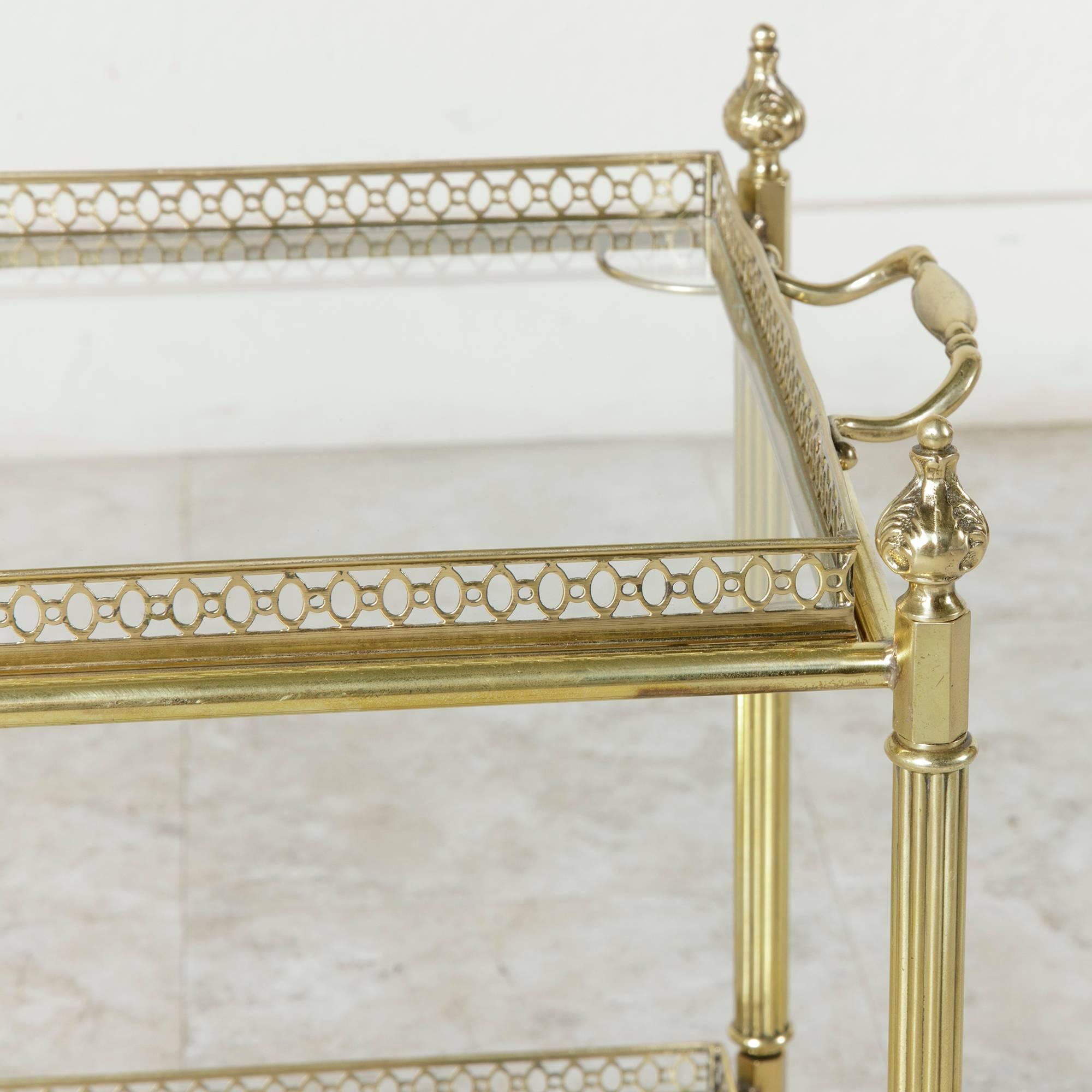 Blending well with all styles and decors, this Mid-Century brass Louis XVI style side table from France features fluted legs topped with finials as well as two removeable glass trays surrounded by brass galleries. A versatile piece, this side table