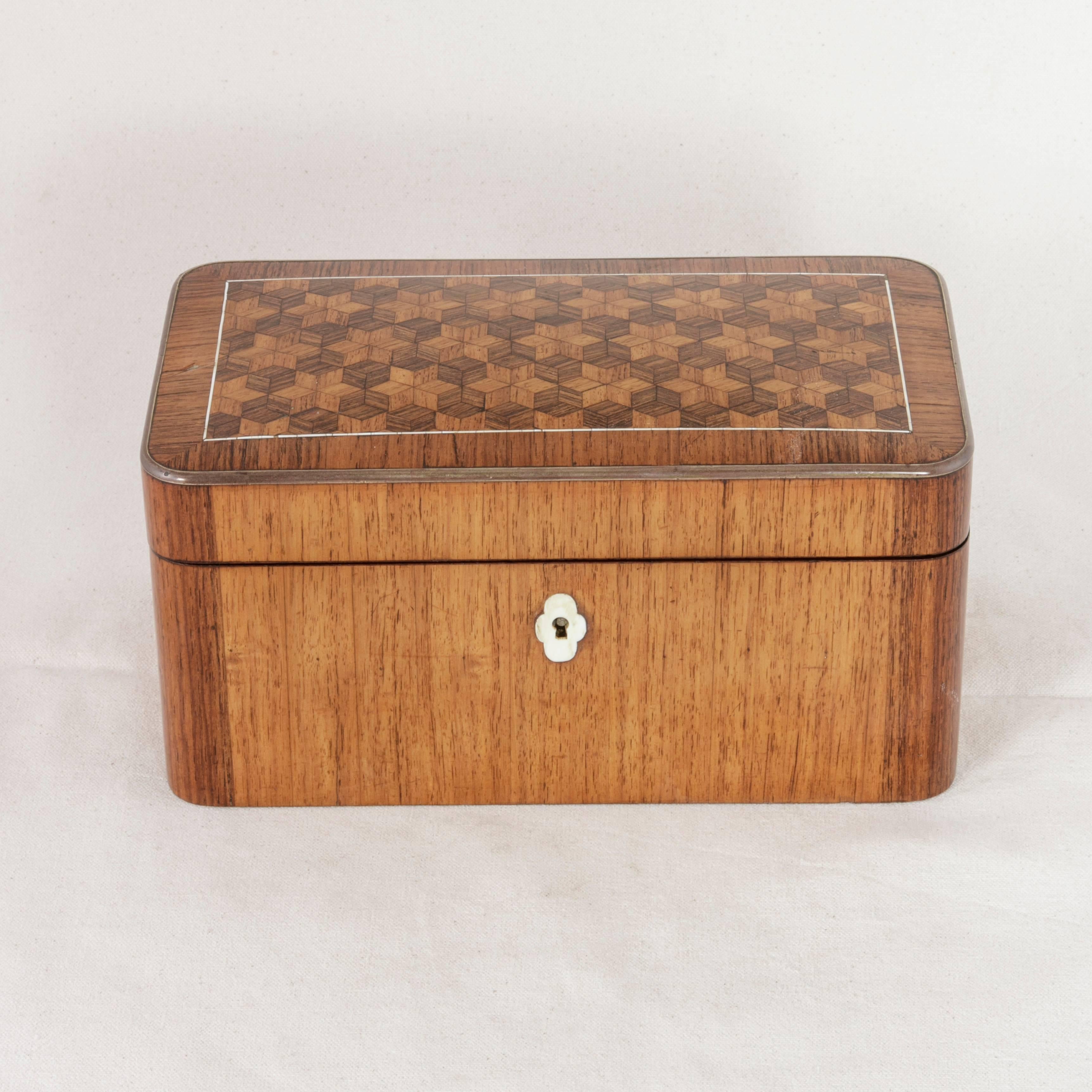 This 19th century, Napoleon III period teabox or tea caddy features marquetry of walnut and rosewood in an intricate hexagram pattern surrounded by a delicate line of bone inlay which complements the bone key surround. Bronze edging around the top's