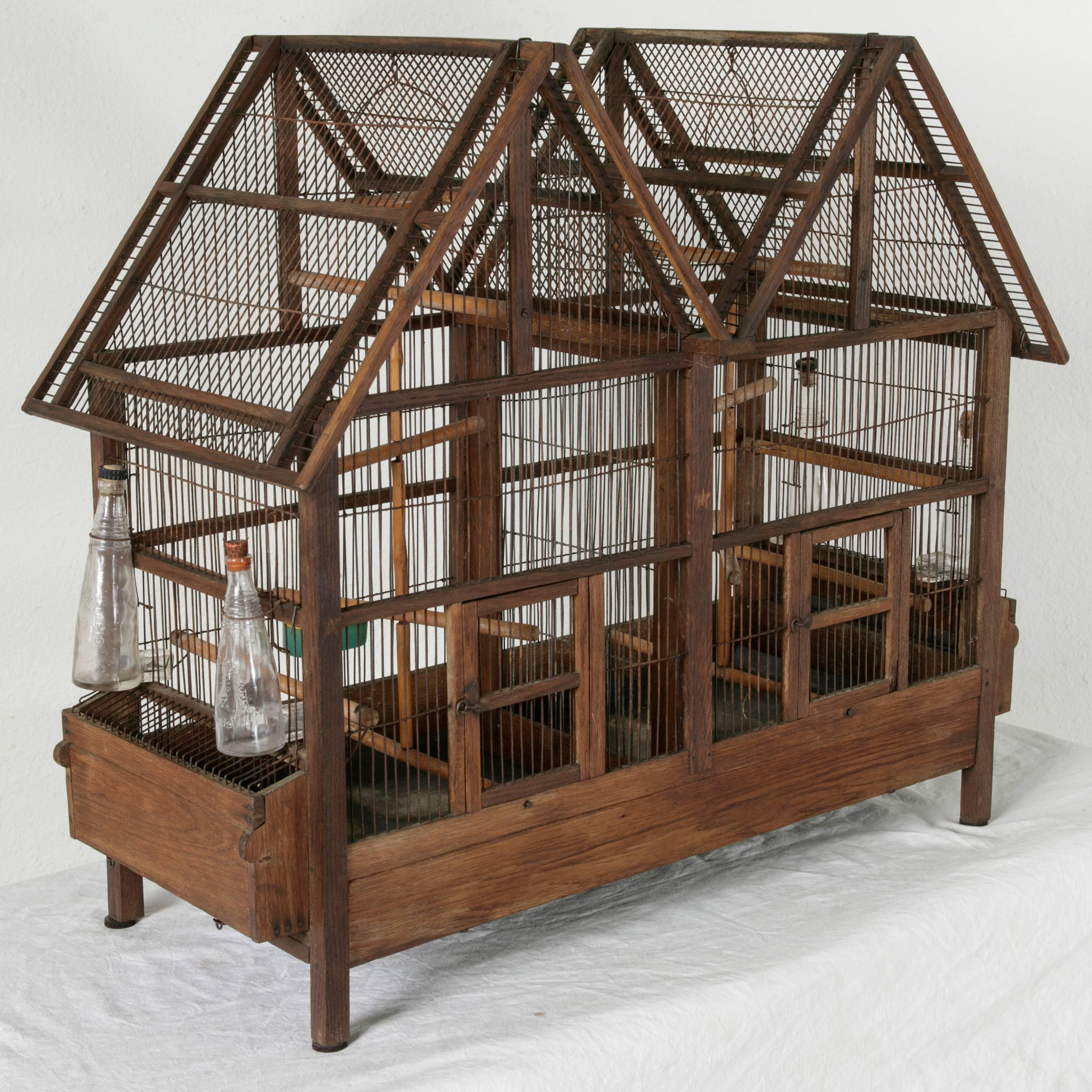 This very large artisan-made wood and wire bird cage takes the form of a double gabled house and features a removable zinc bottom and twelve different perches. With two compartments that can be joined by removing the central wall, each side has its