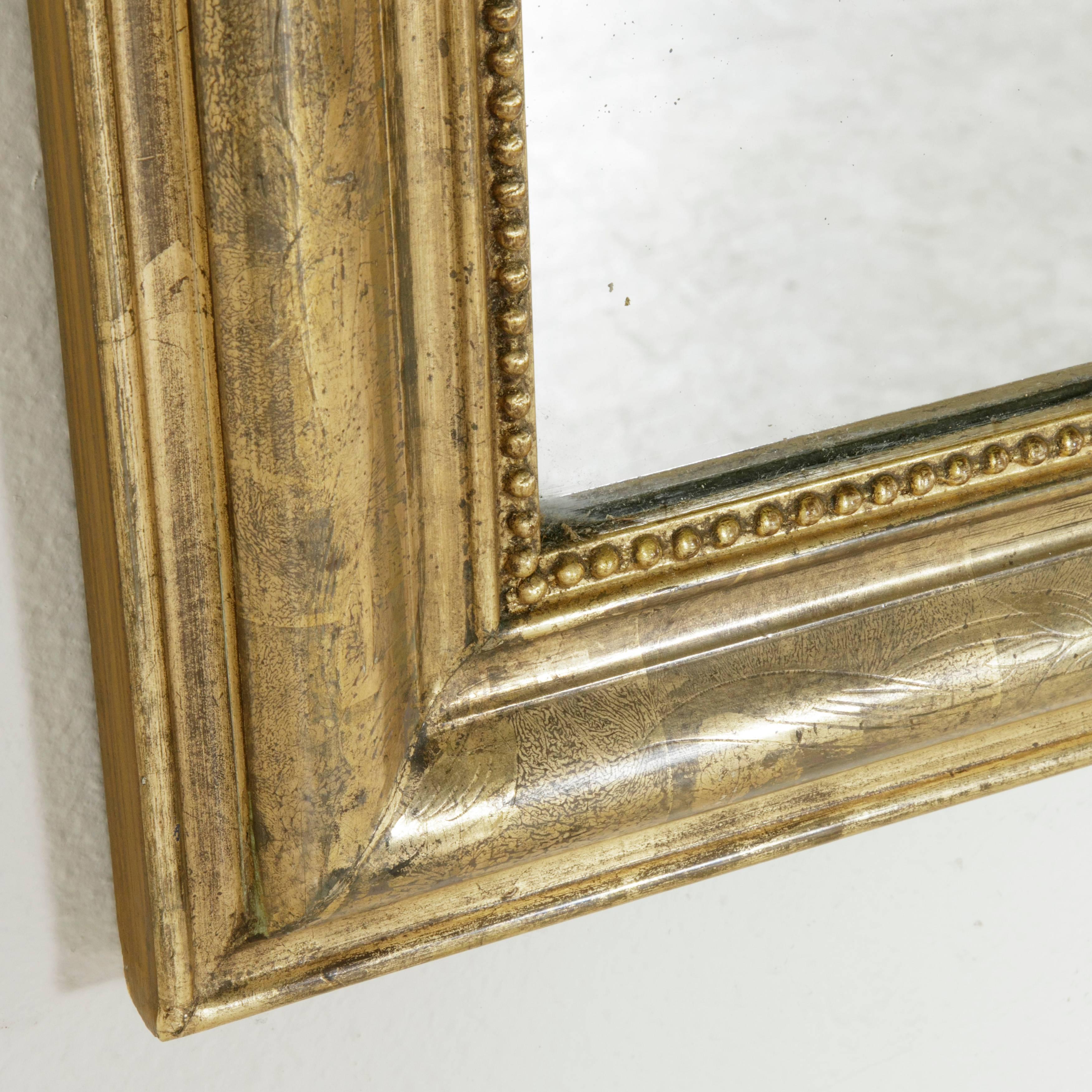 With clean lines and classic look, this nineteenth century Louis Philippe style giltwood mirror boasts its original mercury glass and a beautiful bronze color. The frame features an intricately incised pattern of leaves on its gold leafed water gilt