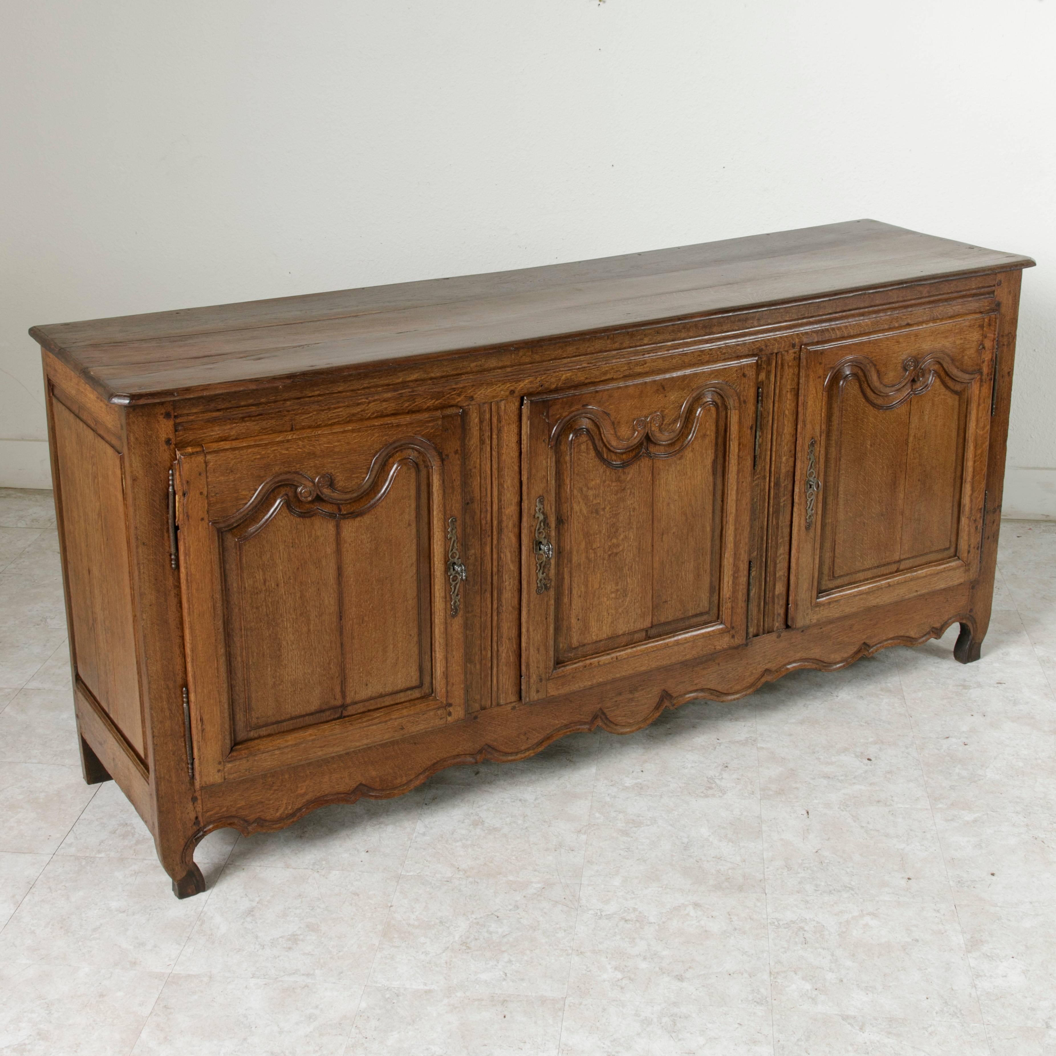 This beautifully hand-carved oak Louis XV style enfilade or sideboard from the early nineteenth century features three doors and an interior shelf that runs the entire length of the piece. Finished with a beveled top and hand-carved panels of