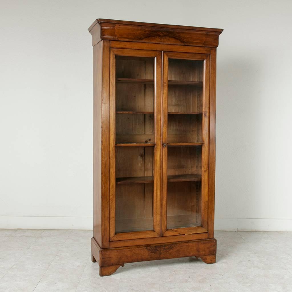 With clean lines and a simple style that blends with all interiors, this Louis Philippe period bookmatched burl walnut bibliotheque or bookcase features its four original handblown glass panes and solid walnut panels on the sides. Four adjustable
