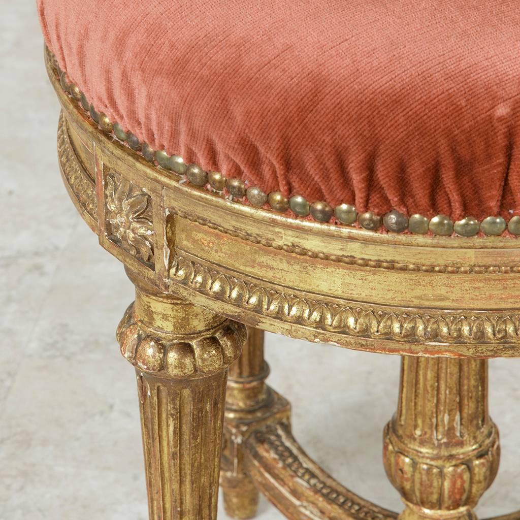 Upholstered in dark blush colored mohair and finished with nailhead trim, this French Louis XVI style giltwood vanity stool from the mid-nineteenth century features rosettes on the die joints. Four fluted legs are joined by two half circles that