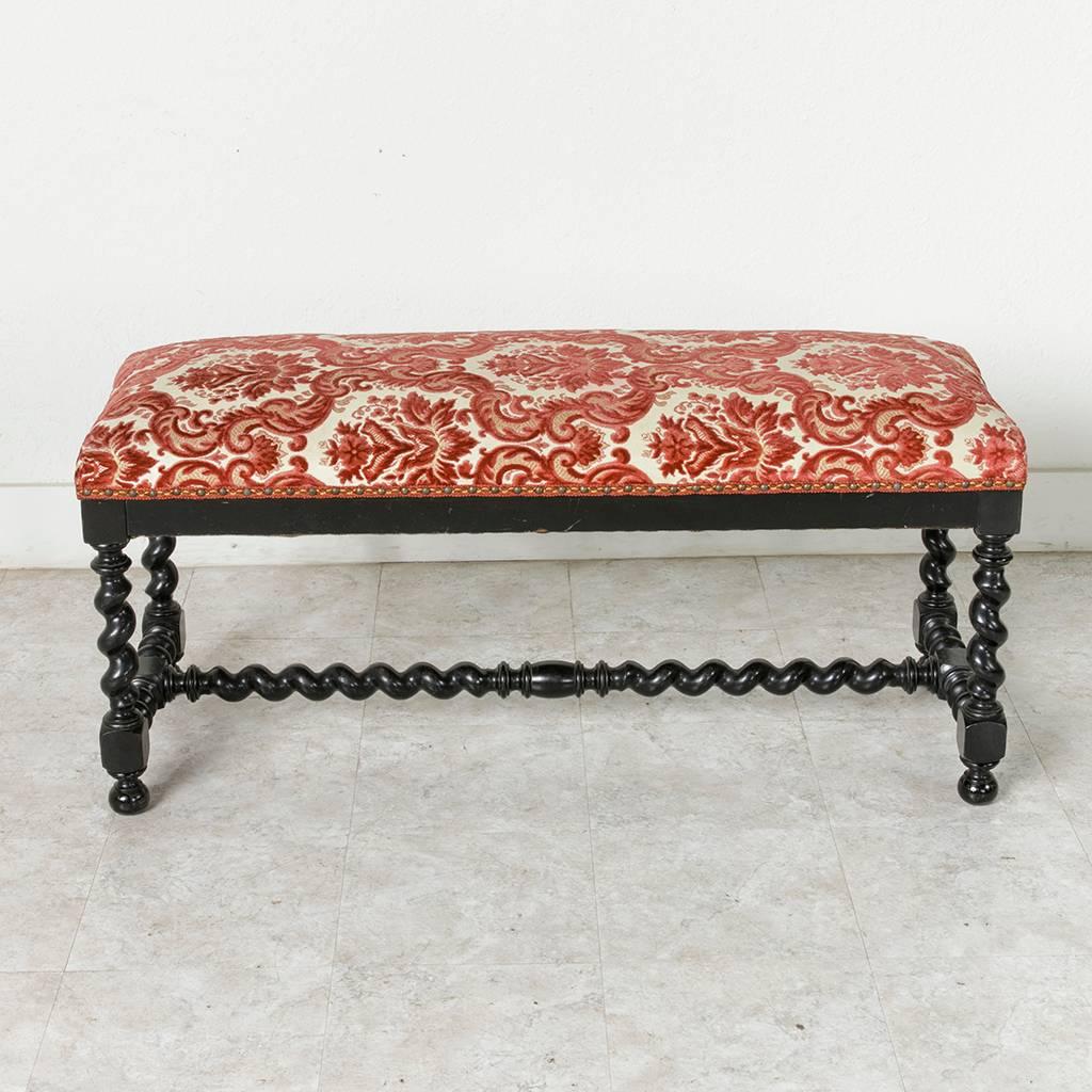 This mid-19th century French Louis III style ebonized banquette or bench features barley twist legs and three barley twist stretchers that provide structural stability. Resting on ball feet and upholstered in red and white with nailhead trim, this