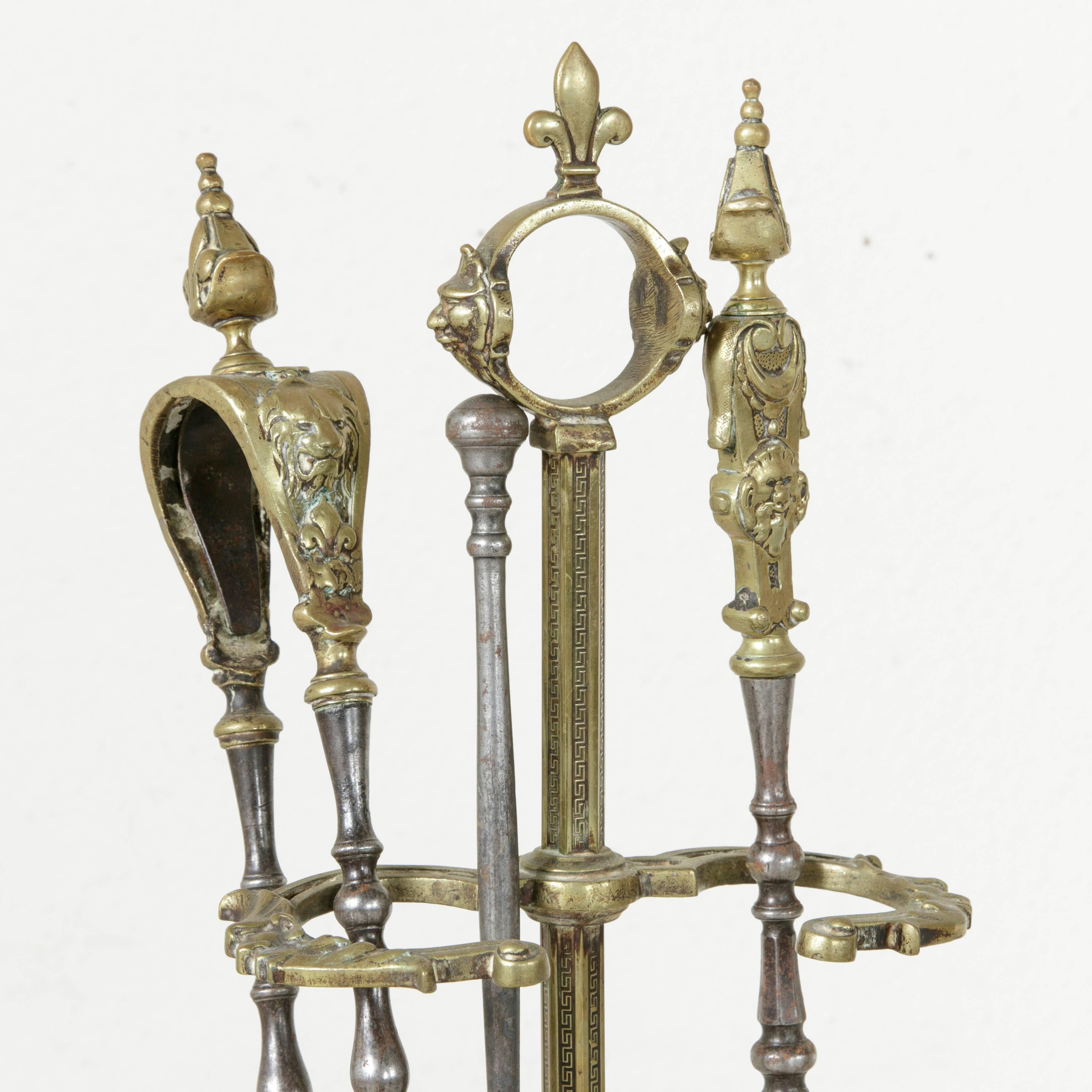 This set of late 19th century bronze fireplace tools is complete with a stand, poker, shovel, and tongs. The stand features a heptagon shaped base with detailing of a leaf surrounded by scrolling. Bands in a Greek key pattern run the length of the