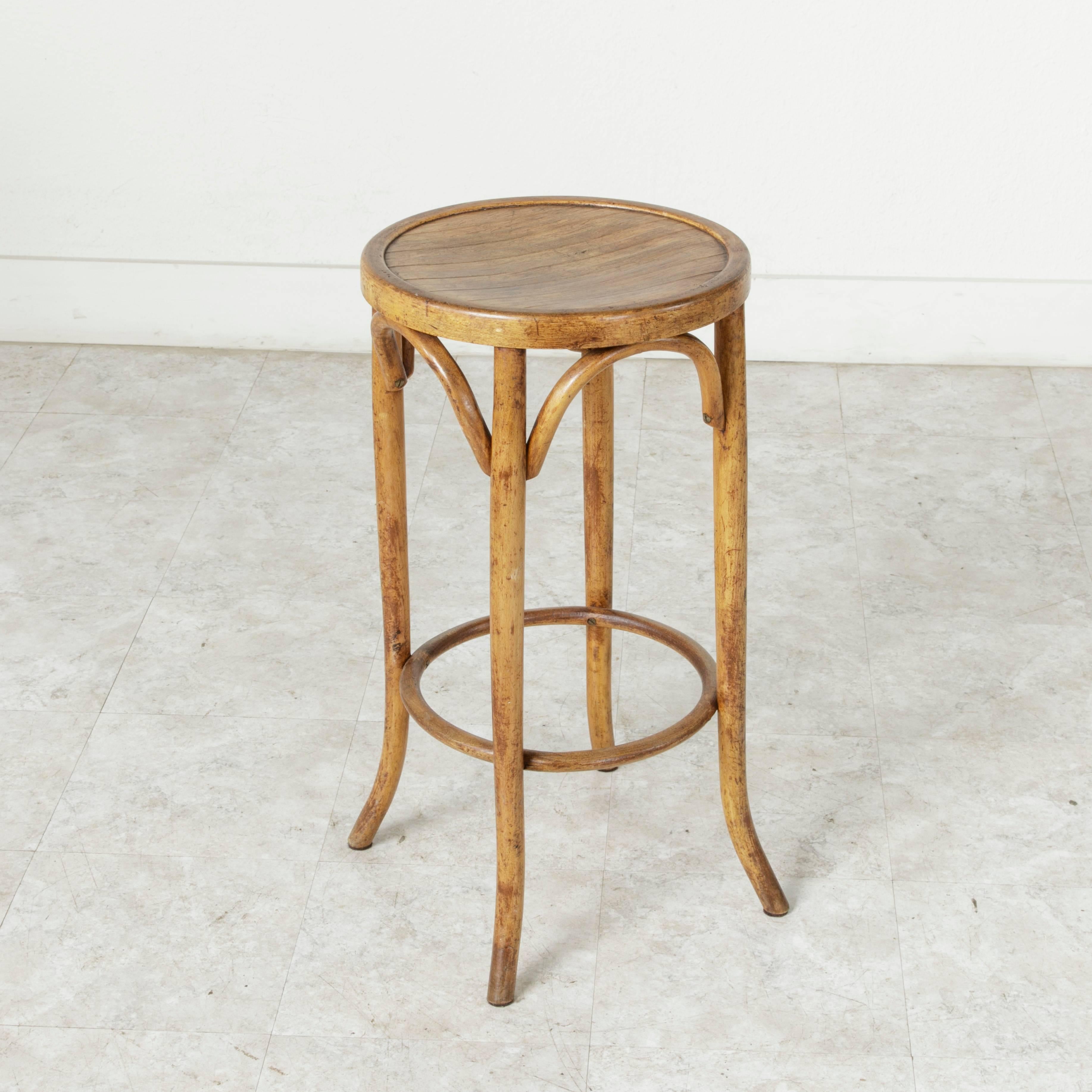 This early 20th century French bar stool in the Thonet style stands at counter height. Constructed of bentwood, this backless stool features a slatted seat and a circular stretcher at the bottom that acts as a footrest. Curved wood arches at the top
