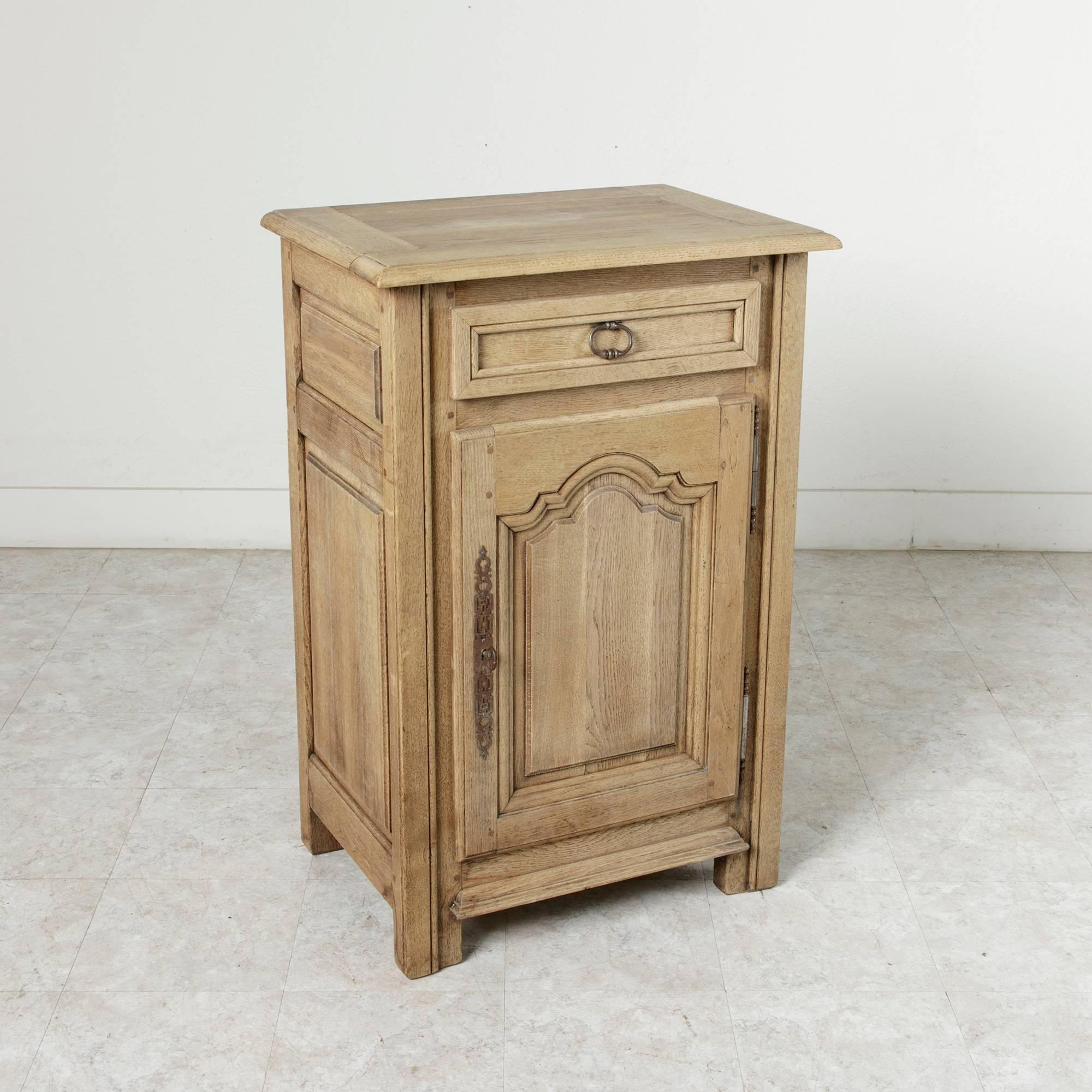 This hand-carved oak French jam cabinet bears its natural finish. Executed in the Louis XIV style with stout, straight lined legs and a symmetrically arched paneled door, its heavy style is juxtaposed by its light finish. Each side features raised