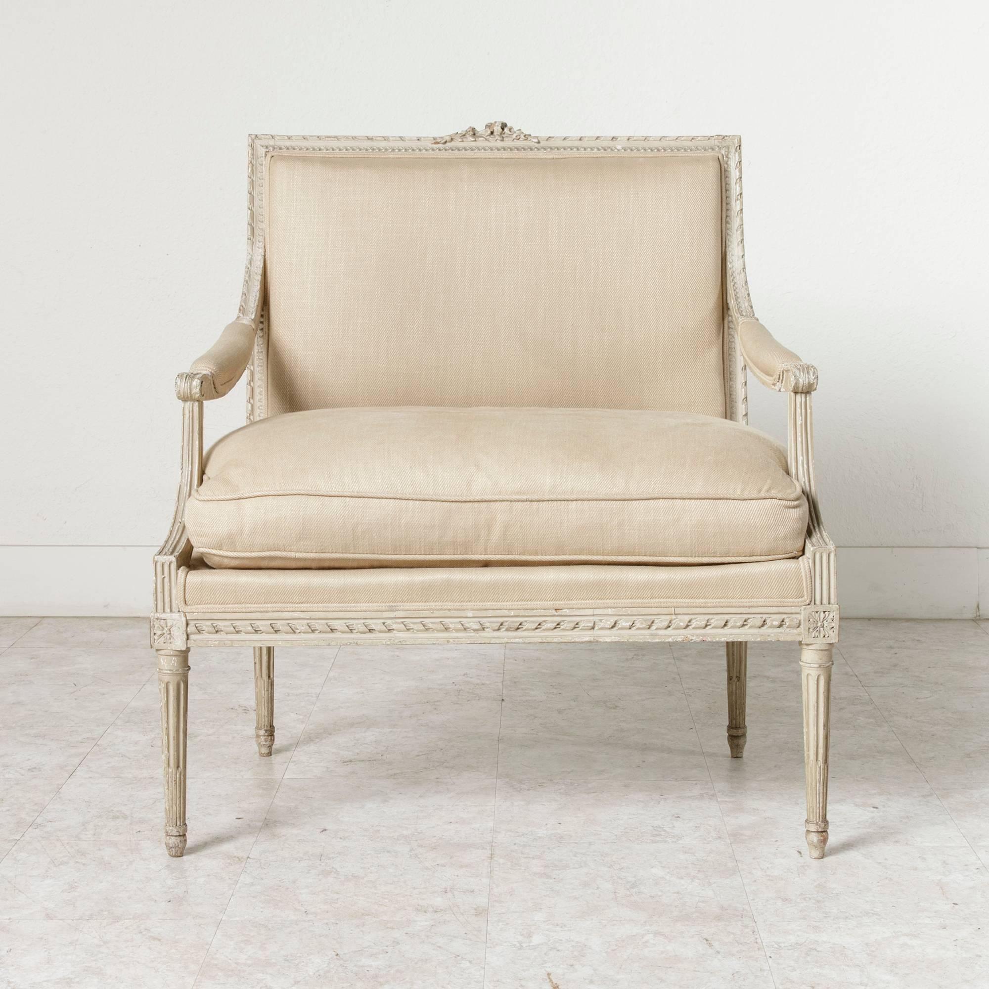 With a unique width of 33 inches, this Louis XVI period painted armchair, called a fauteuil a la reine (armchair for a queen), was originally meant to accommodate the large dresses worn by noble women of the period. Its delicate hand carvings