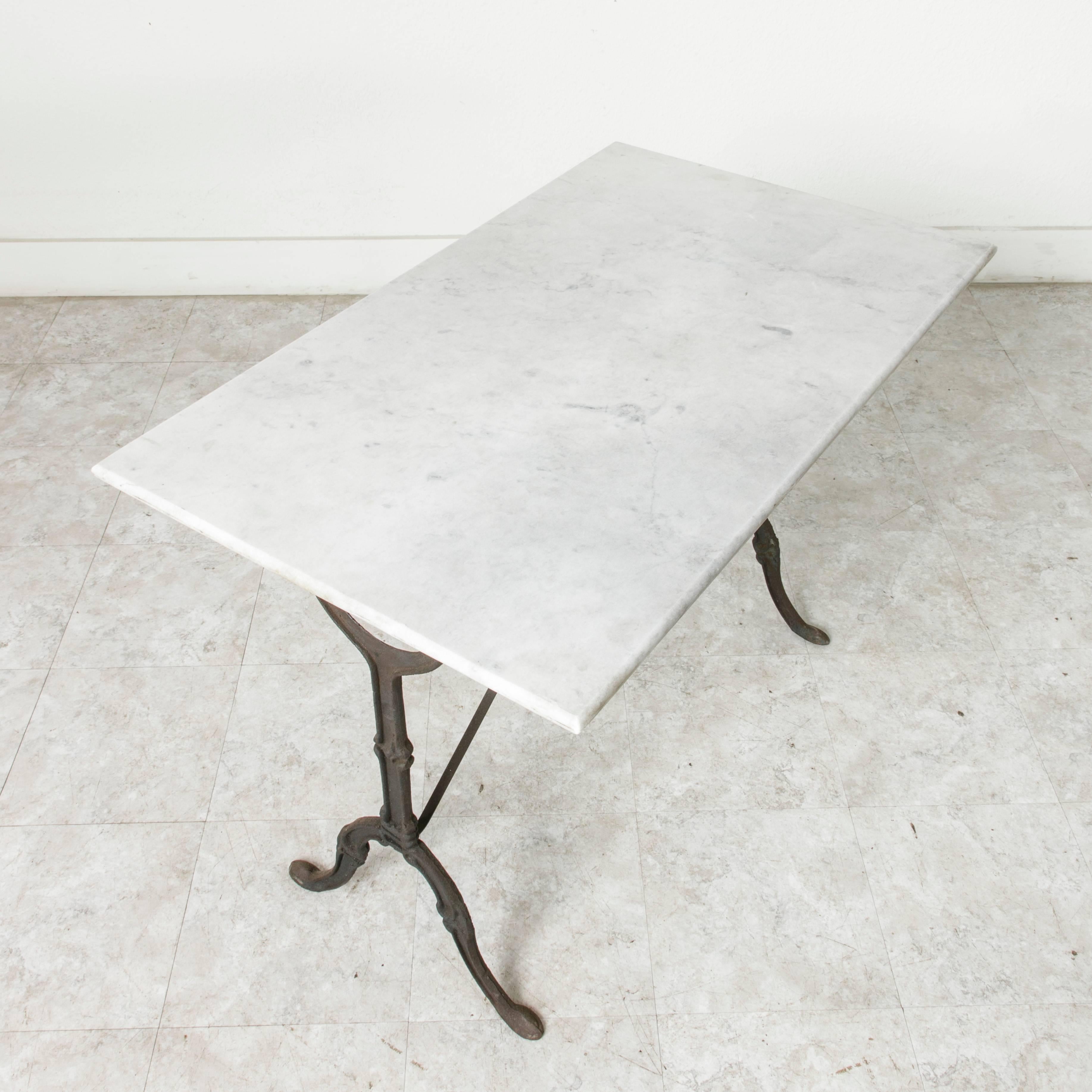 This mid-20th century cast iron bistro table features its original solid marble top held in place by an iron peg on each side. A riveted stretcher provides additional stability. Ideal as a garden table or in a breakfast nook, this Classic French