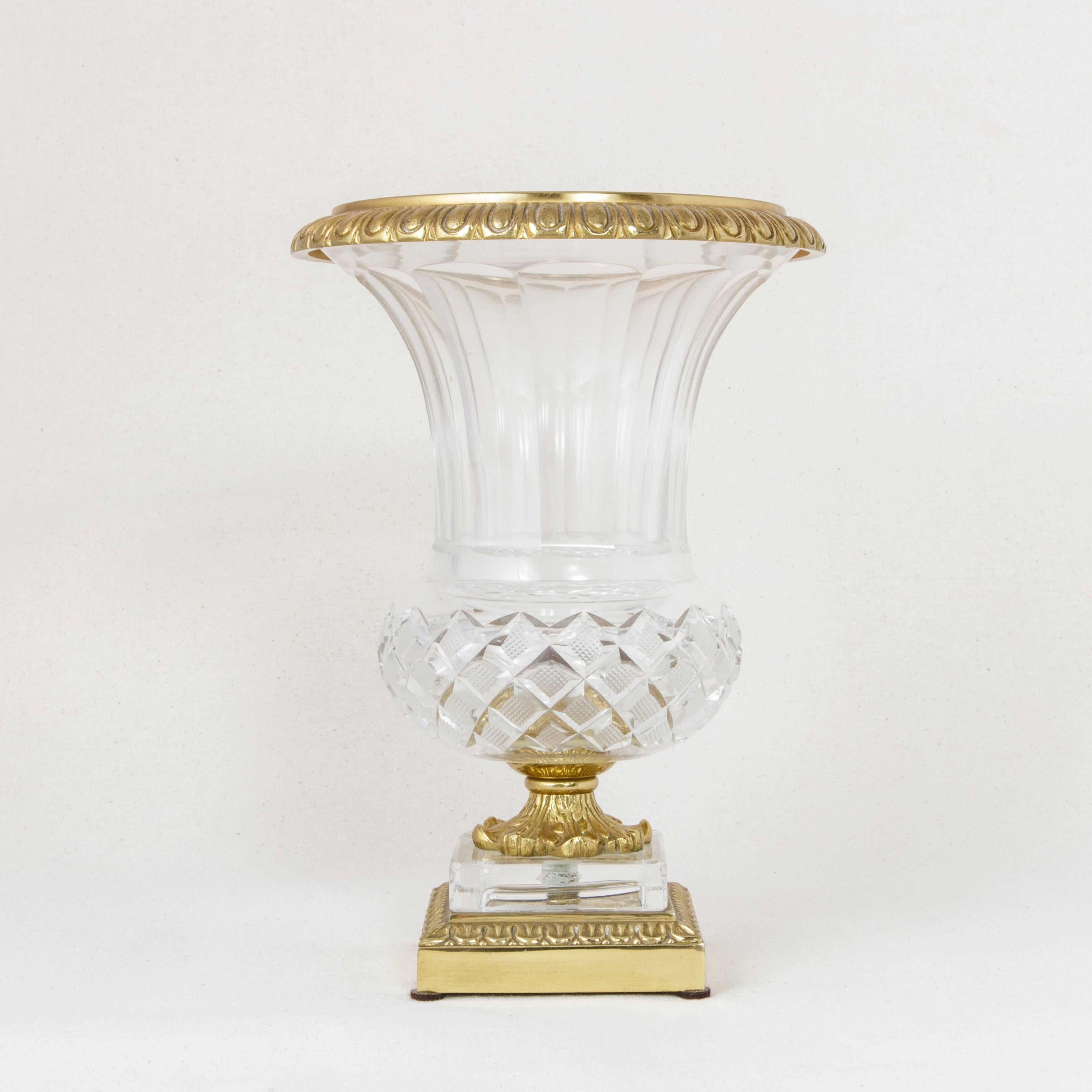 An elegant cut-glass piece from the Art Deco period emulating a Classic Medicis urn, this vase features a hand-cut grid pattern, fluted sides, and an upper bronze rim. It is mounted on a bronze stem of draped acanthus leaves supported by a glass