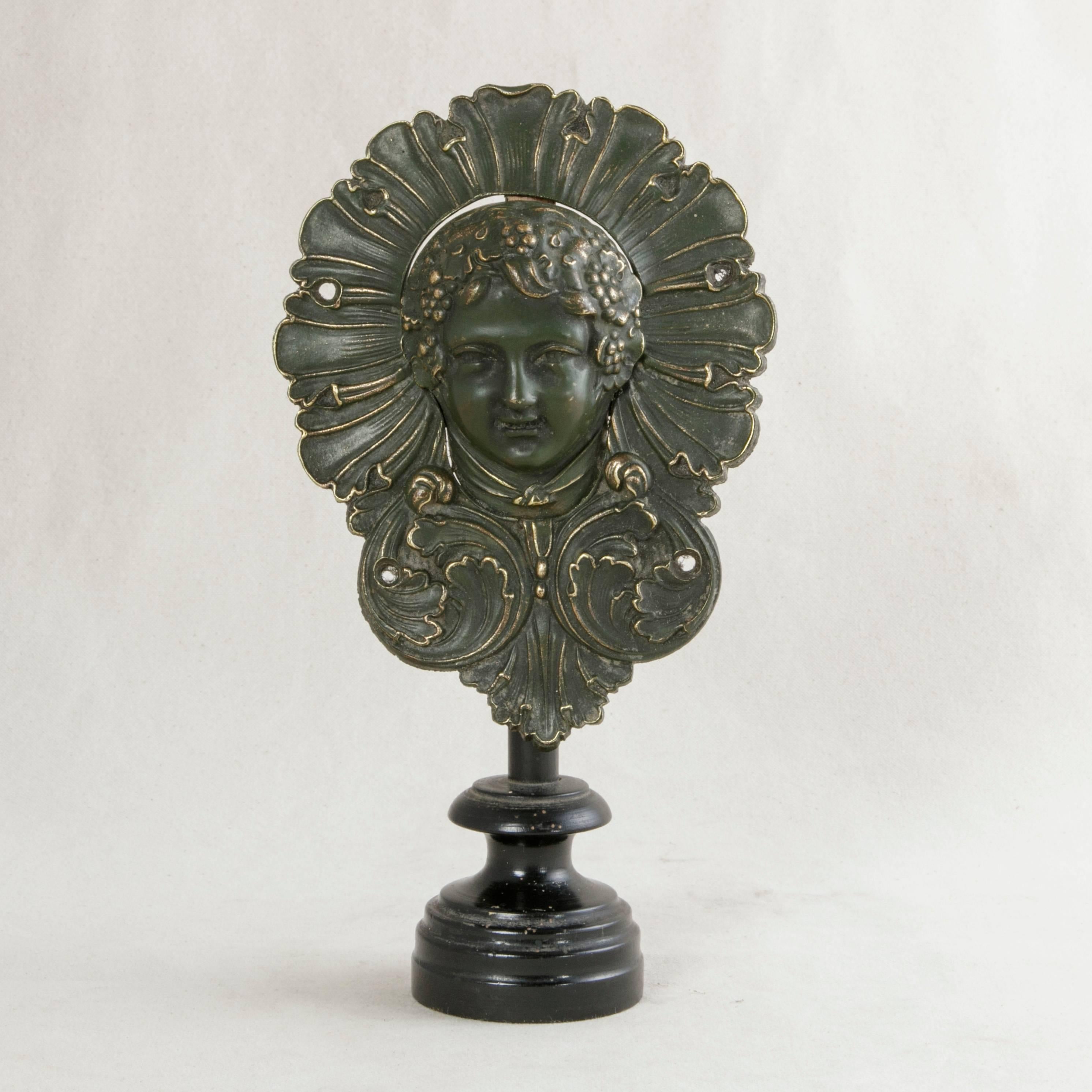 Bacchus, the god of wine, is presented in bronze in this unusual billiard pocket from the Napoleon III period. This smiling face, wearing a crown of grapes and grape leaves surrounded by a halo of stylized petals and acanthus leaves, originally