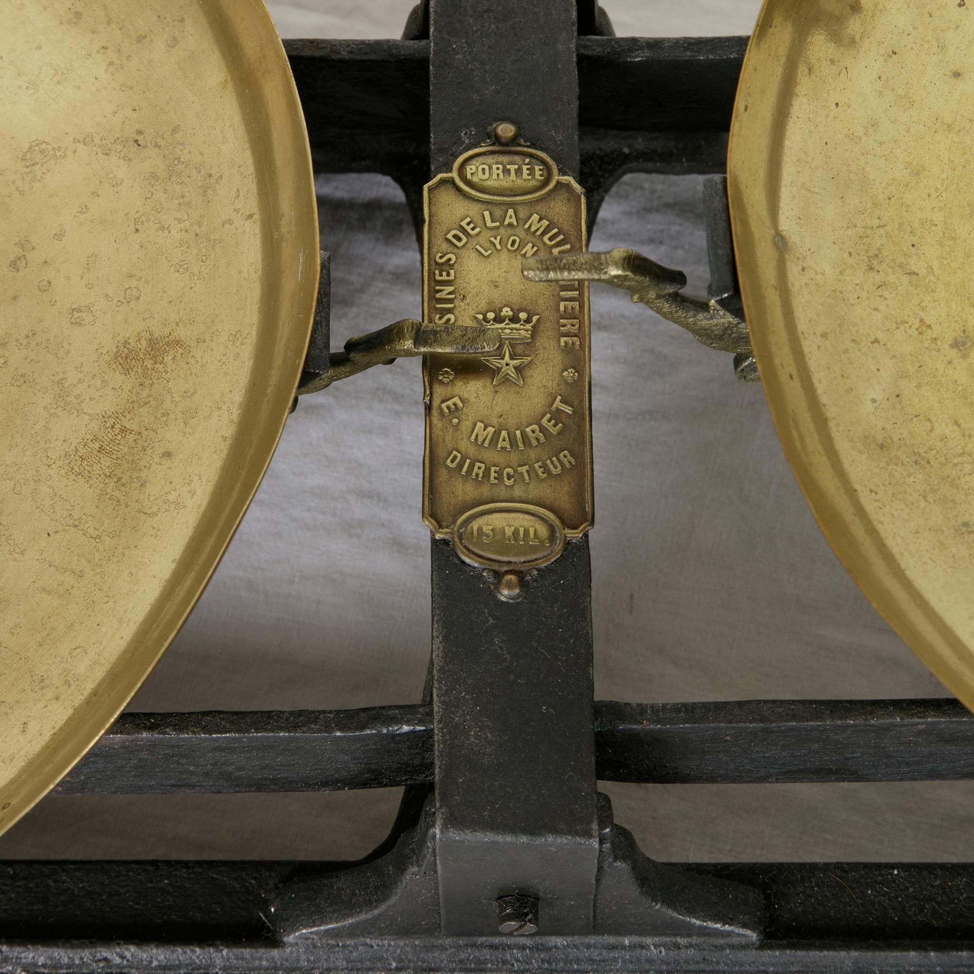 This set of late 19th century baker's scales features a leaf motif around its iron base and two ten-inch diameter brass pans. Its original brass label is marked Usines de la Mulatiere, Lyon E. Mairiet Directeur, Portee 15 kilos, indicating the