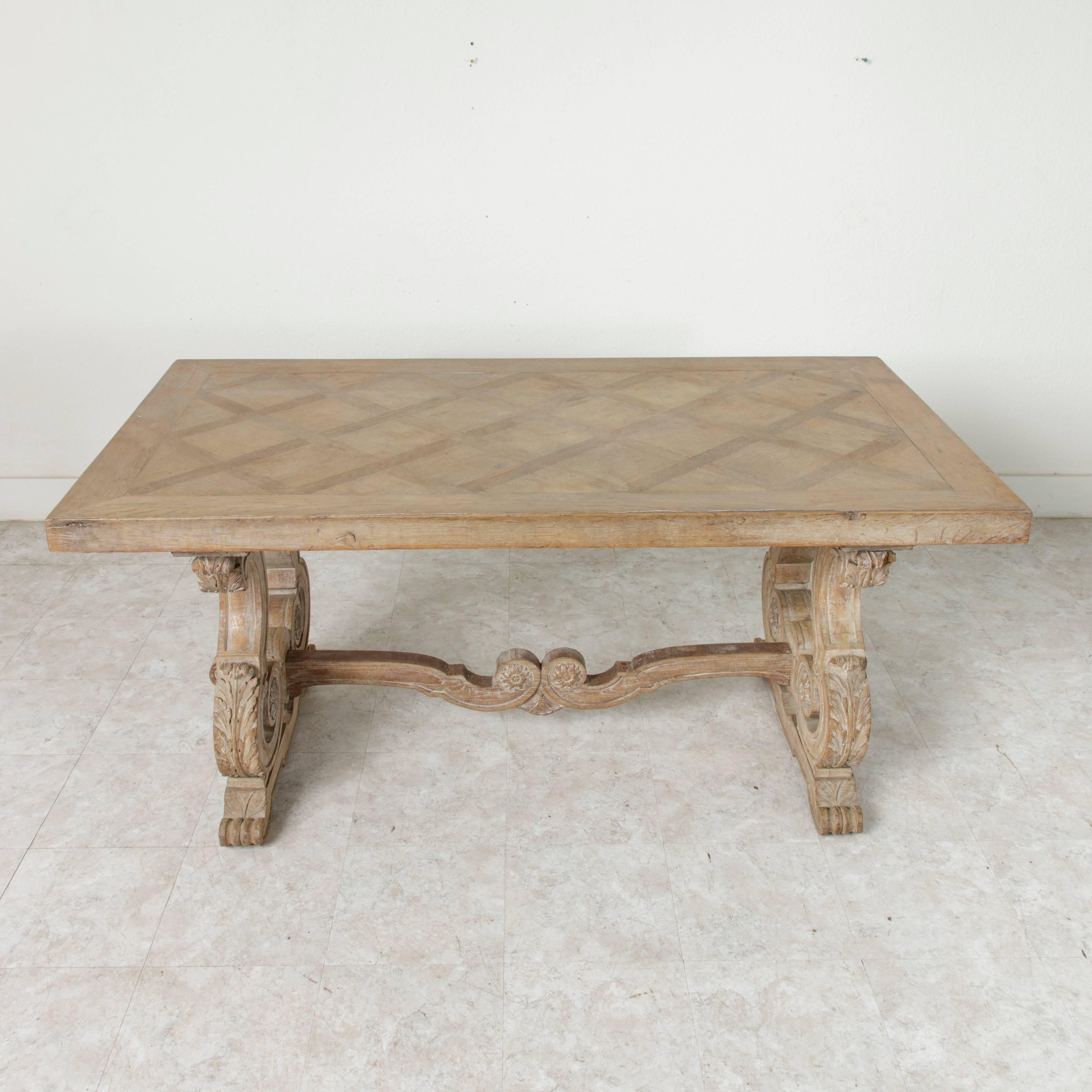 With a natural finish in the Gustavian Style, this oak table features a hand-carved Renaissance style trestle base from circa 1880. Its cerused legs and stretcher are detailed with carved scrolling ending in rosettes as well as acanthus leaves that