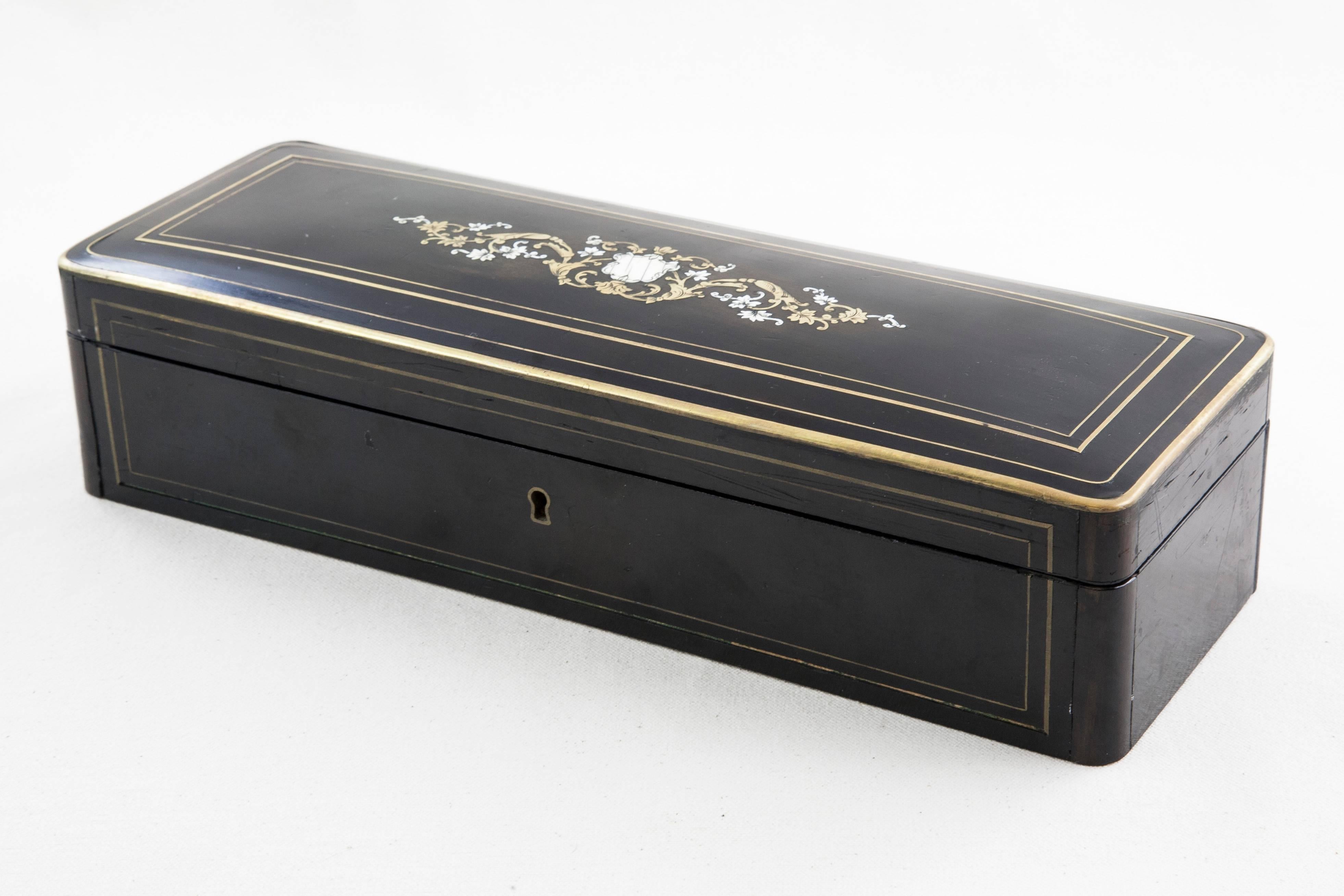 This 19th century Napoleon III period black lacquer jewelry box features an intricate bronze and bone inlaid cartouche on the lid flanked by gadrooning leaves and flowers. Bronze trim lines the top and outer edges of the lid, and a tufted red satin