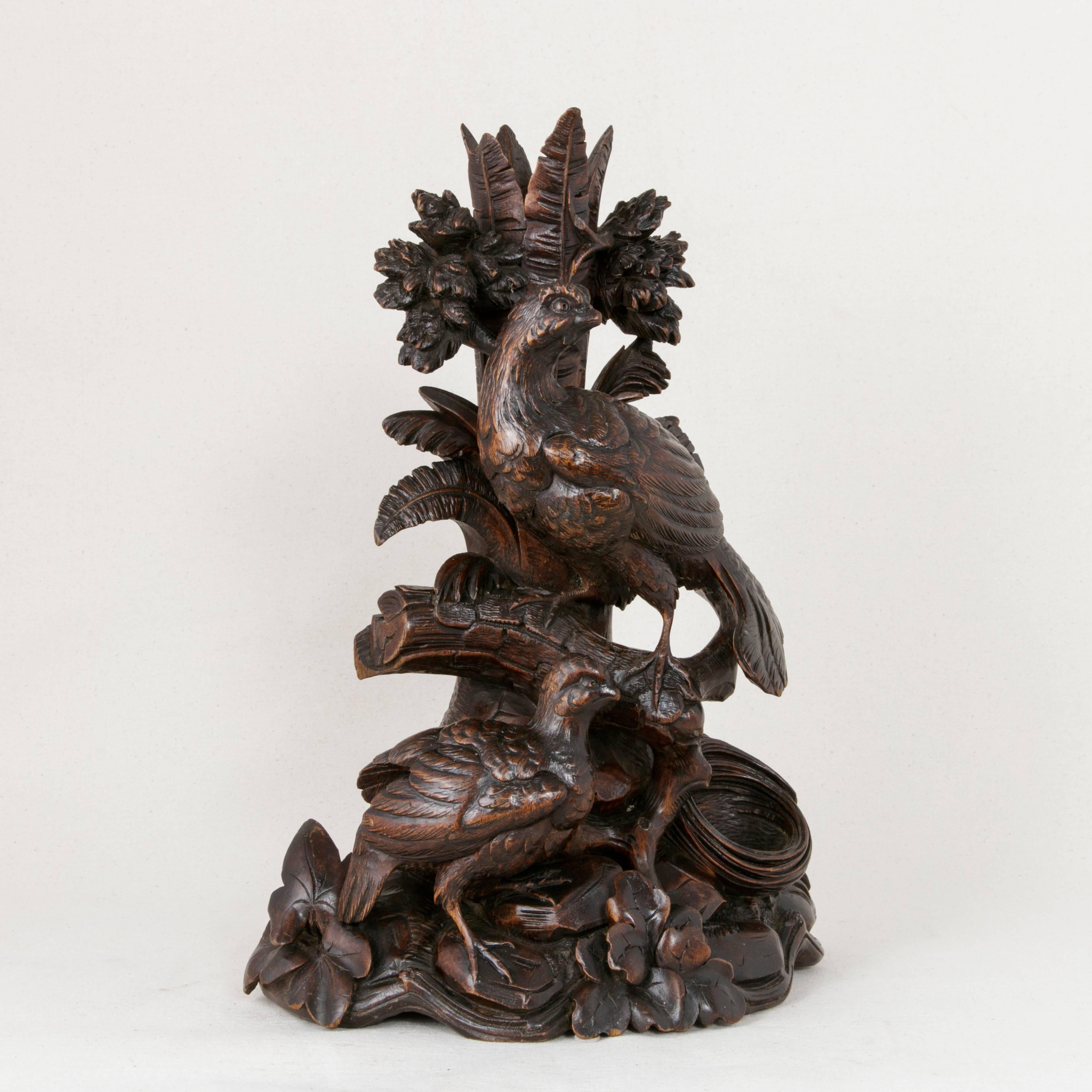 This large hand-carved French Black Forest vase or candlestick features a central tree trunk rising from a rocky base with a pair of grouse game birds perched nearby. An empty nest lays at the base of the tree. Large leaves extend upward from the