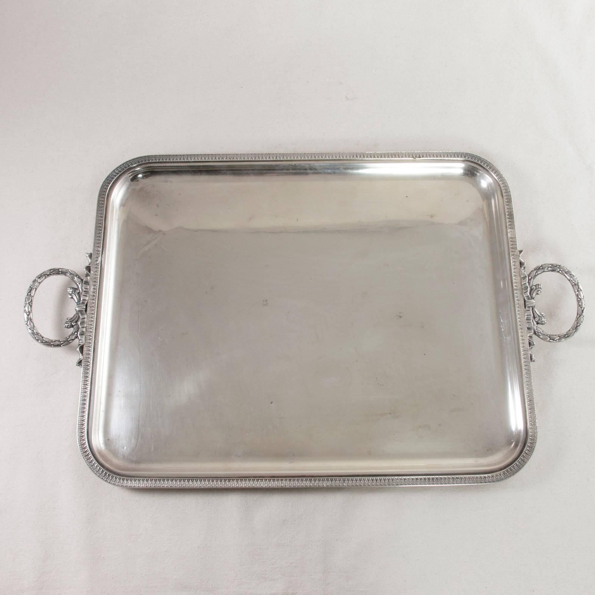 This Louis XVI style silver plate serving tray from the Art Deco period features a feuille d'eau or water leaf border. Handles on each side are formed by garlands tied together with a ribbon. An ideal piece for any host or Hostess, this silver plate