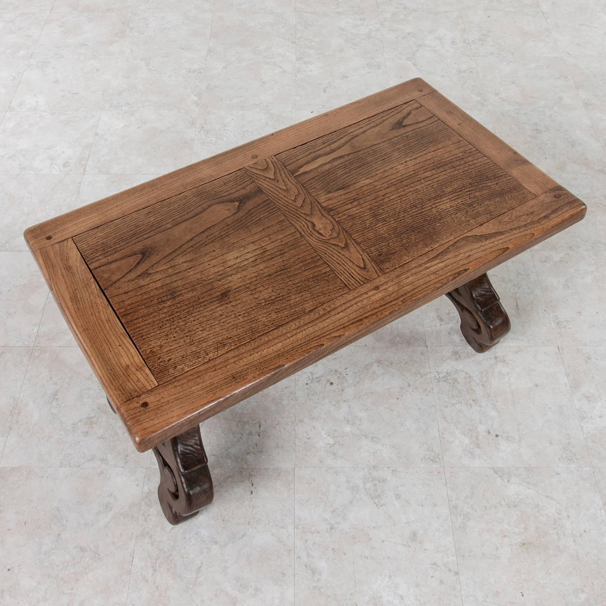 With the warm tones of the wood that give it an old world feel, this Spanish style oak coffee table features a framed top of hand pegged construction mounted on hand-carved lyre shaped trestle legs raised on volutes. A hand-forged wrought iron