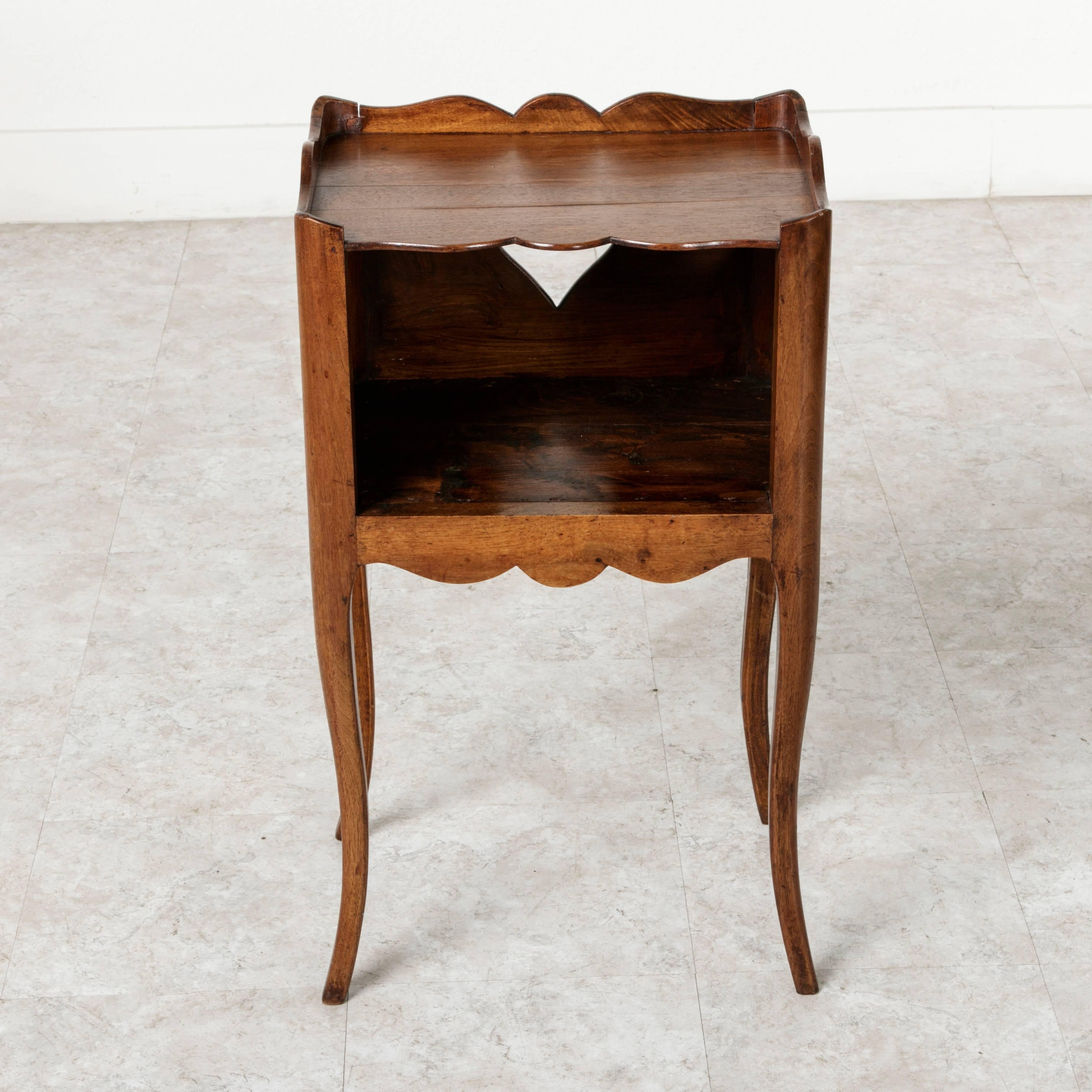 This late 19th century Louis XV style walnut nightstand or side table features elegant cabriole legs and an interior niche. Its top is surrounded by a scalloped gallery on three sides. Cutouts on the sides originally allowed for easier lifting and