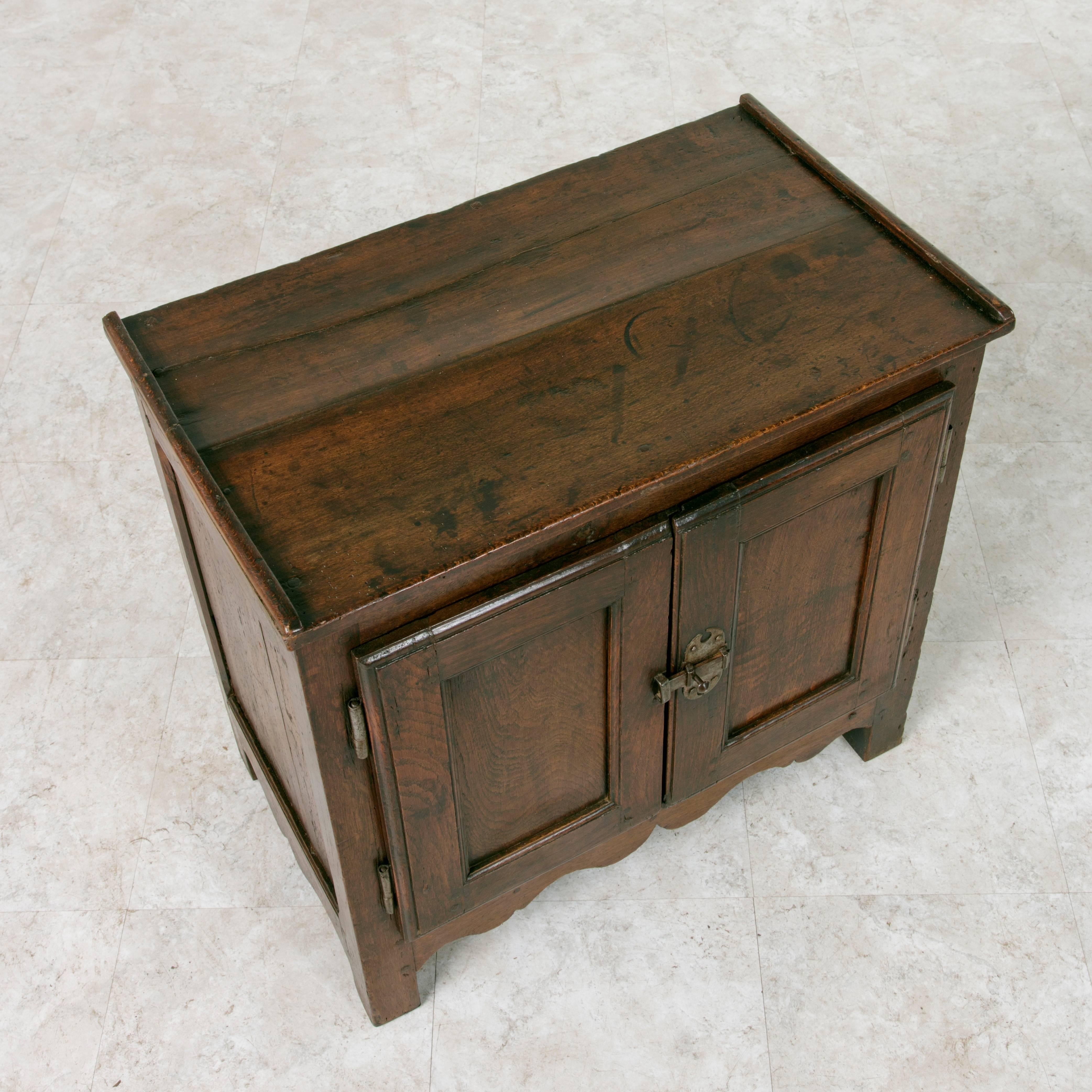 Originally from the region of Normandy, France, this petite 18th century artisan-made walnut cabinet features double doors that close with an iron latch, is complementing its iron hinges. The interior cabinet has a single shelf. This sturdy piece of