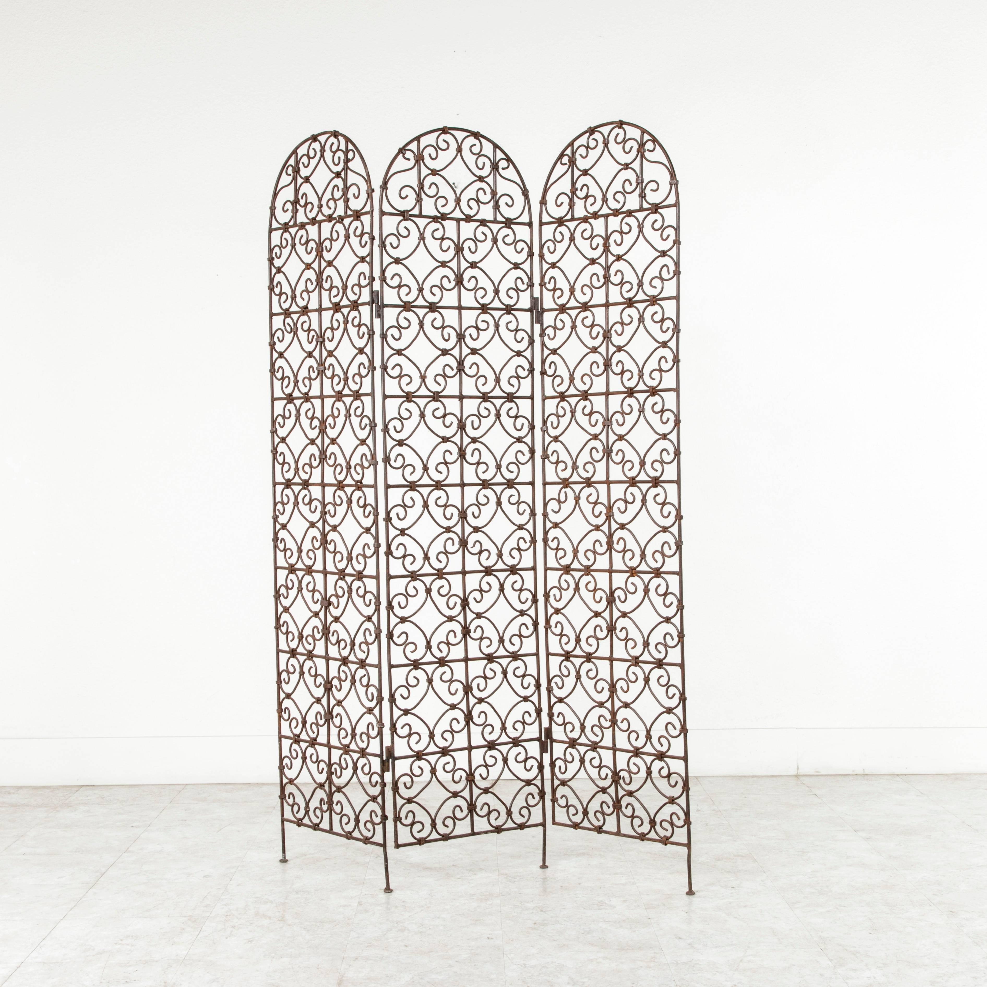 With an intricate hand-forged scrolling pattern, this early 20th century iron folding screen or partition is composed of three panels, each with an arched top. Acquired by a Frenchman in Morocco during the French Colonial period, this artisan-made
