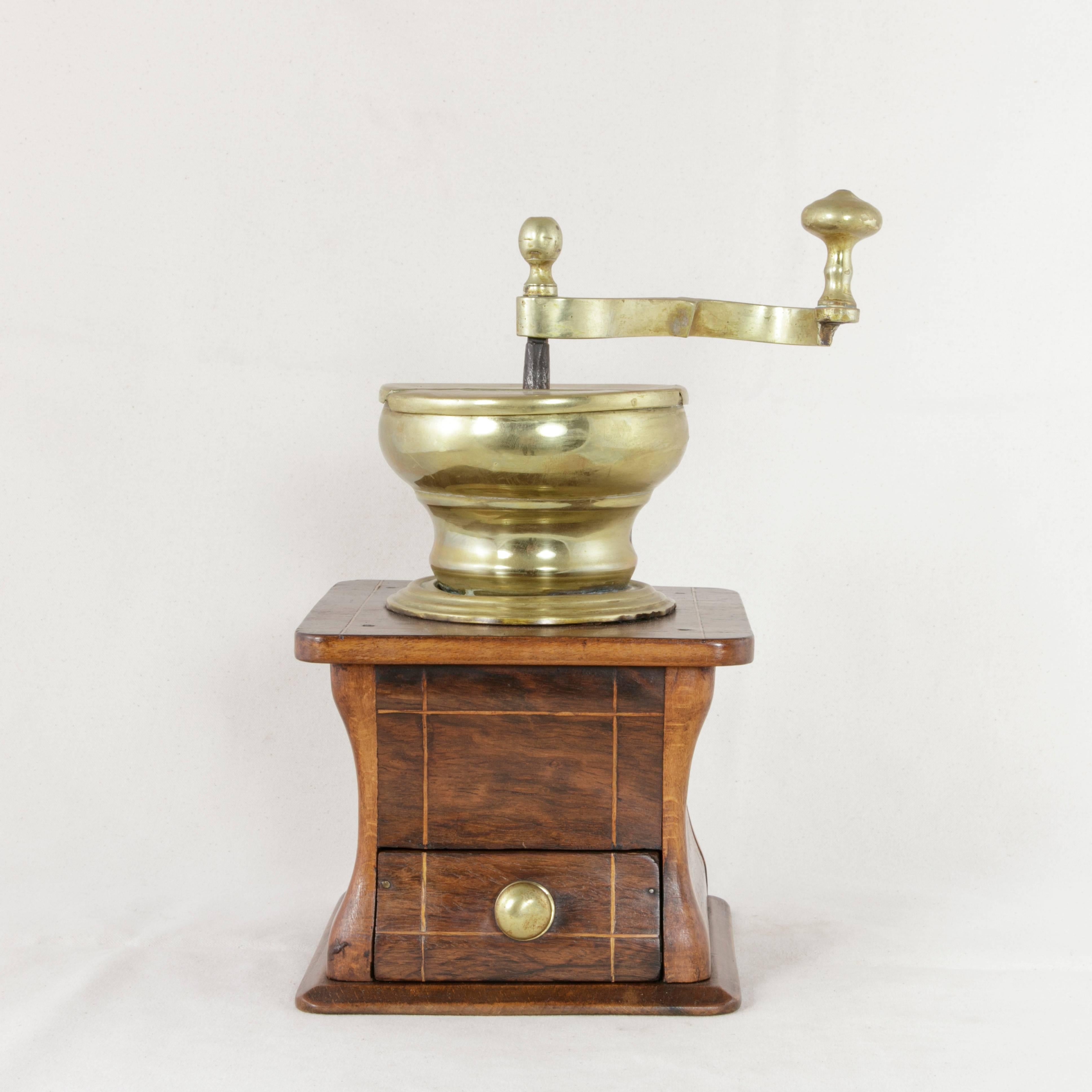 This early 19th century Dutch coffee grinder features a walnut base with fine lines of inlaid lemonwood. A single drawer with a brass knob allows for collection of the coffee grounds. The brass crank mechanism at the top has a hinged lid where