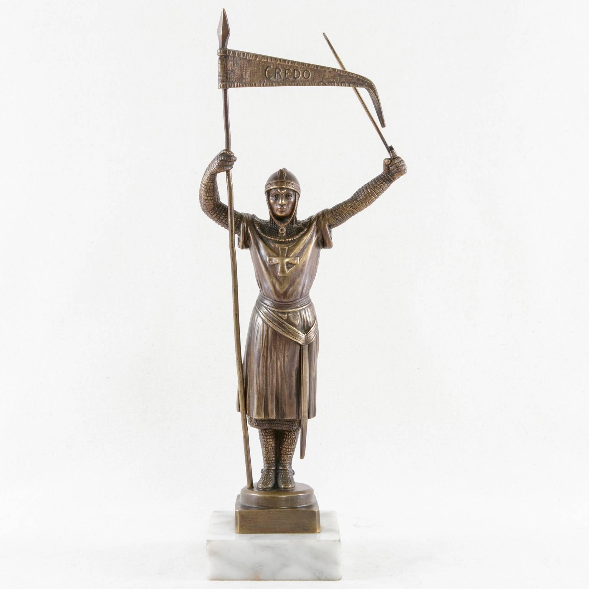 Standing triumphantly atop a white marble base, this Art Deco period bronze crusader of the Order of the Knights Templar holds aloft a sword in one hand and a pennant in the other. Written across the face of his banner is the Latin word Credo