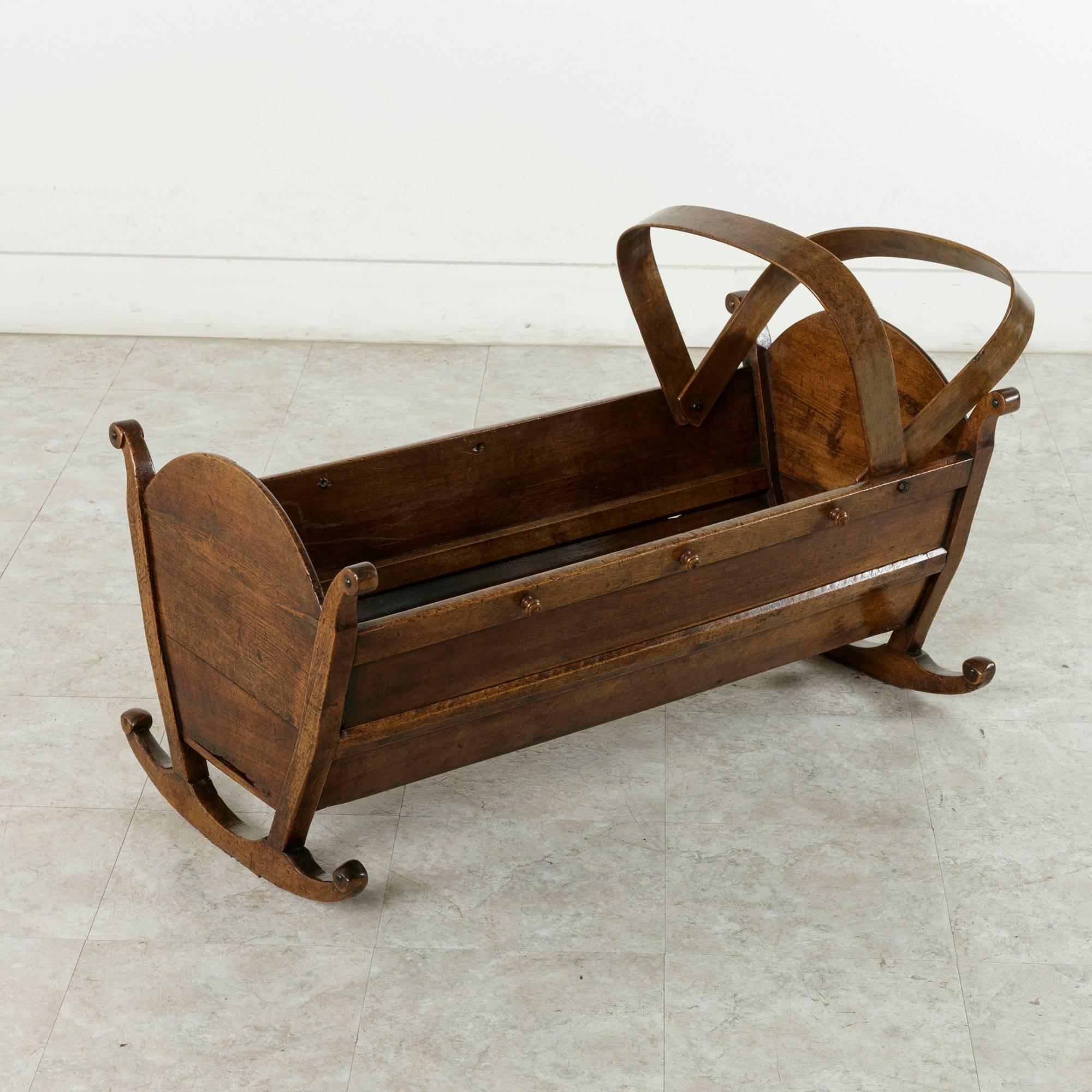 Originally from the region of Savoie, France, near the Swiss border, this mid-nineteenth century hand-carved walnut cradle rests on two scrolled rockers. Wooden knobs on each side of the cradle were originally used to attach leather straps that
