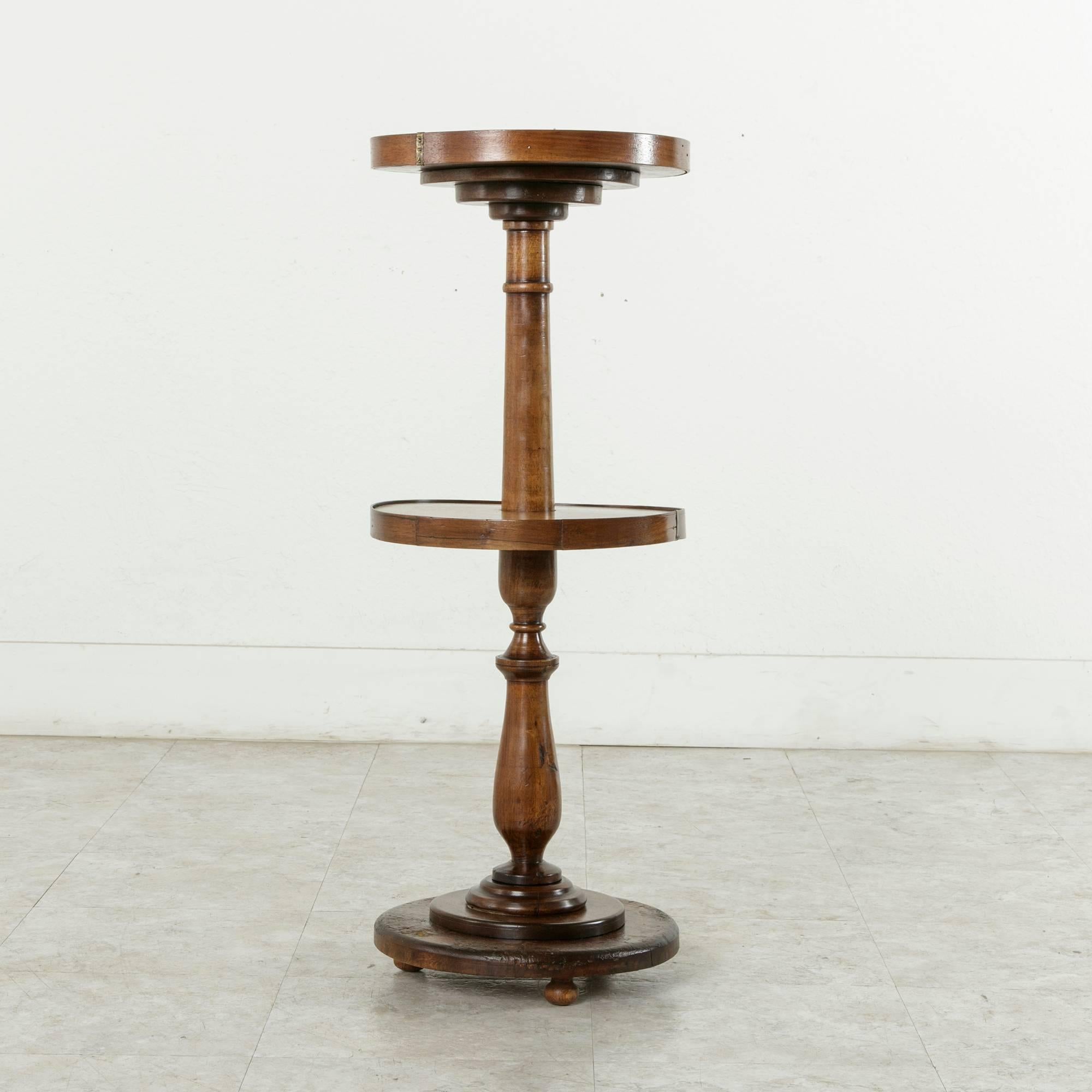 This two-tiered walnut pedestal was originally a lace maker's table in the 19th century. The lower tier turns freely and once held multiple wooden bobbins used by the lace maker. She would turn the table platform to the bobbin of thread needed as