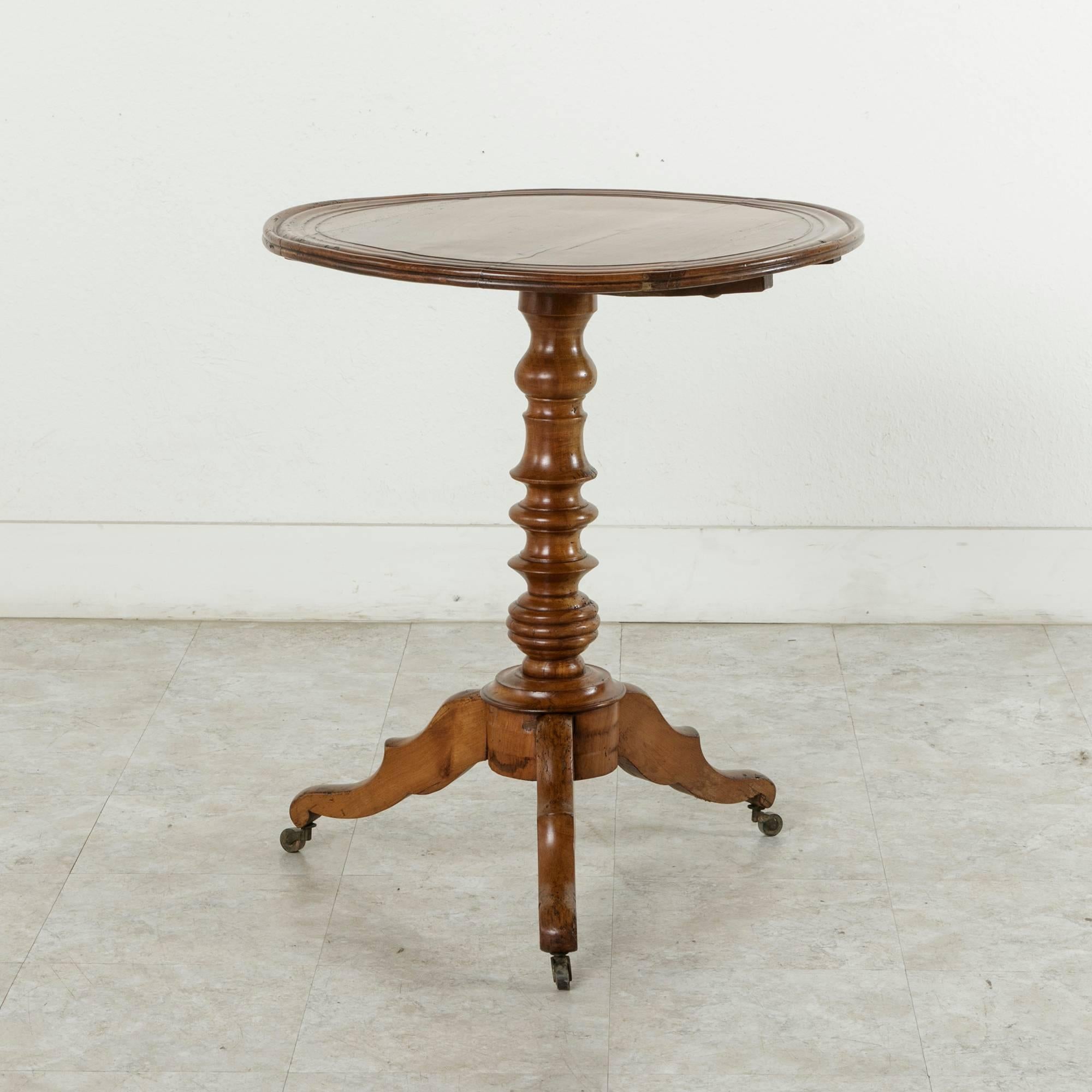 Constructed of cherrywood, this French Louis Philippe period pedestal side table features a double beveled tilt top that rests on a central turned pillar. The column is supported by a tripod base with casters on the feet. An ideal table to place