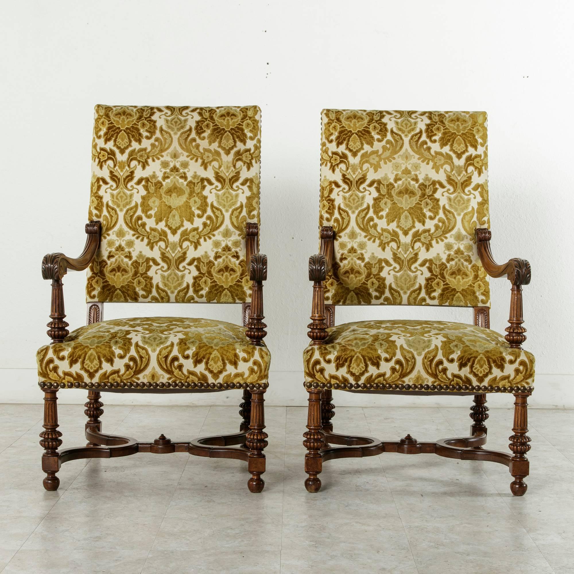 This pair of large-scale French walnut Louis XIV style armchairs from the late nineteenth century feature hand carvings of scrolling acanthus leaves on the armrests which are supported by fluted columns. Additional leaf carvings adorn the supports
