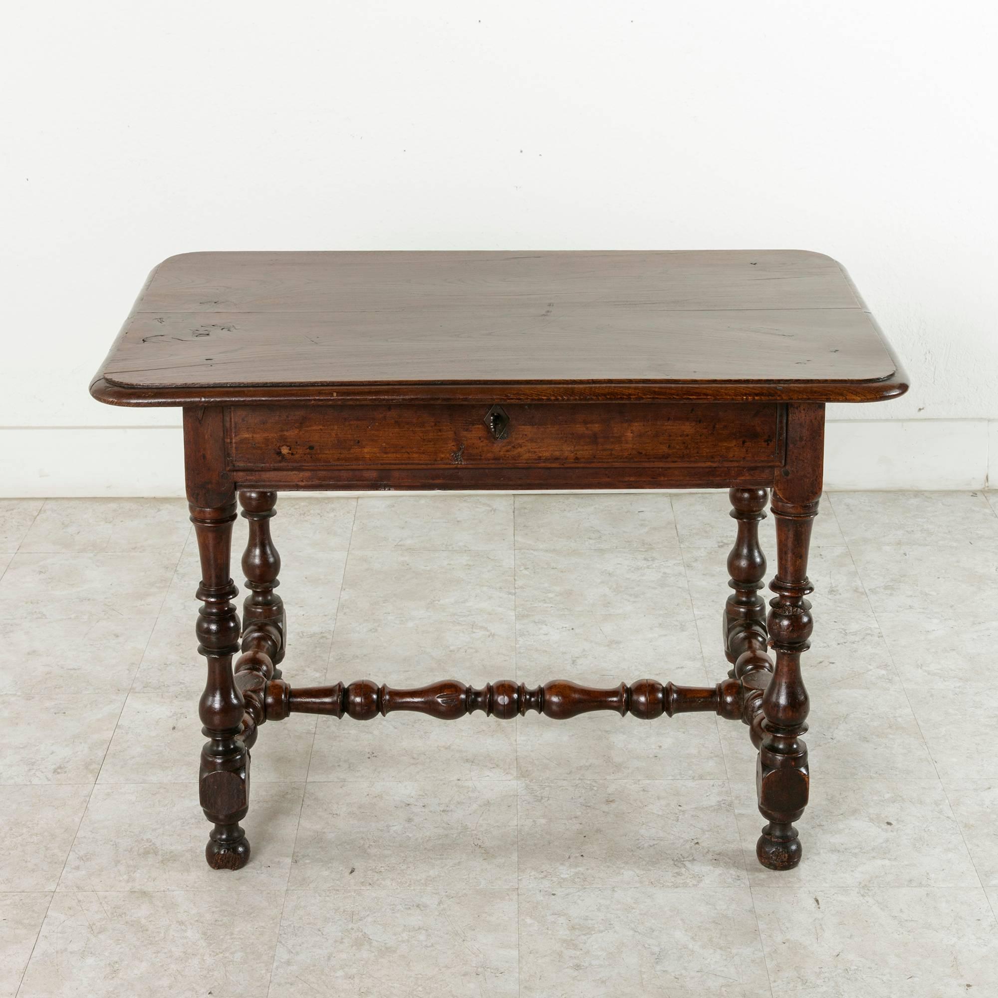 This Louis XIII style hand pegged oak table from the late 18th century features turned legs resting on ball feet and joined by an H-stretcher. Its top is made of two 14 inch wide planks, and its single drawer of dovetail construction is finished