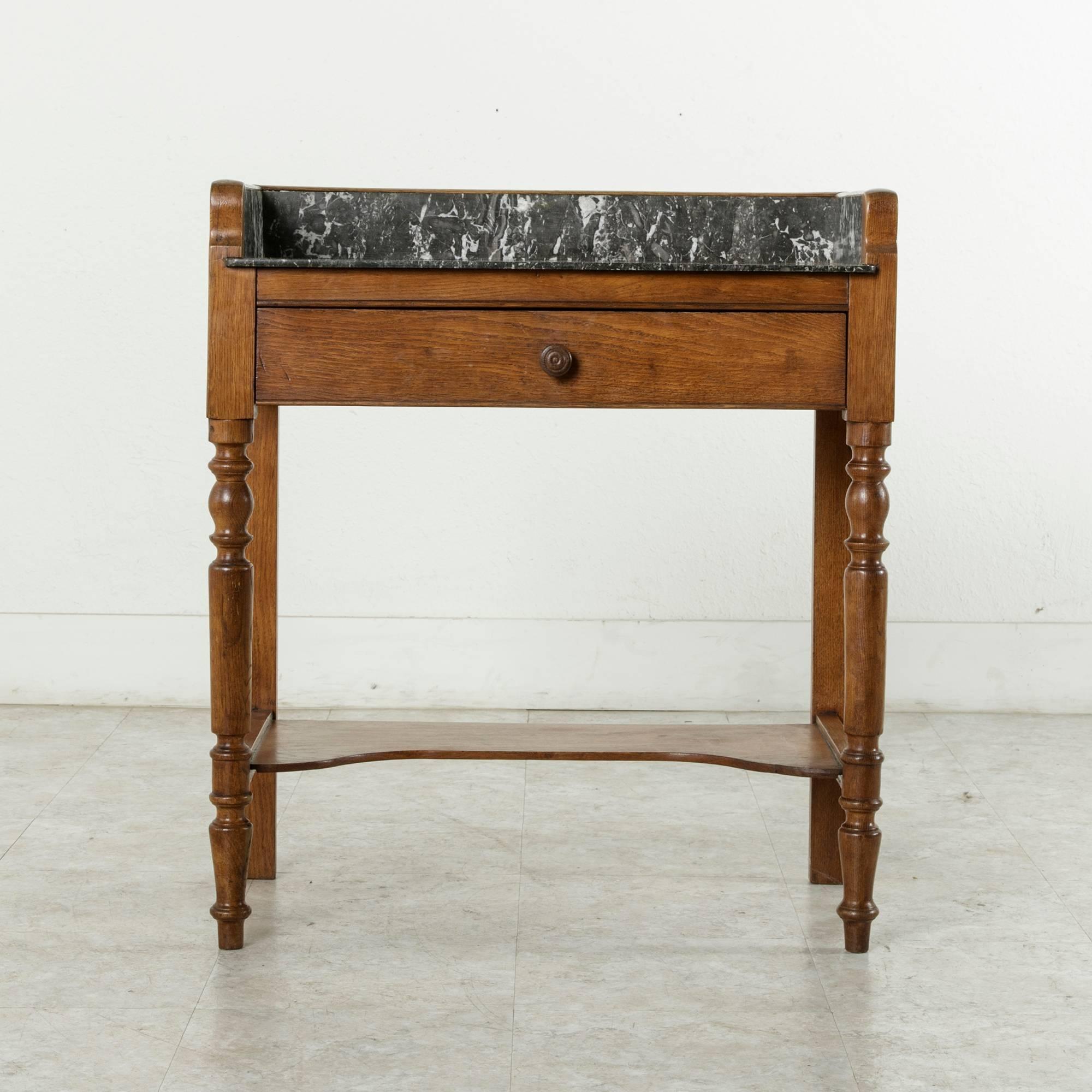 This late 19th century oak console table features a Saint Anne marble top and a marble surround on three sides. A single drawer of dovetail construction extends between the two turned legs in the front. A lower shelf provides extra stability as well