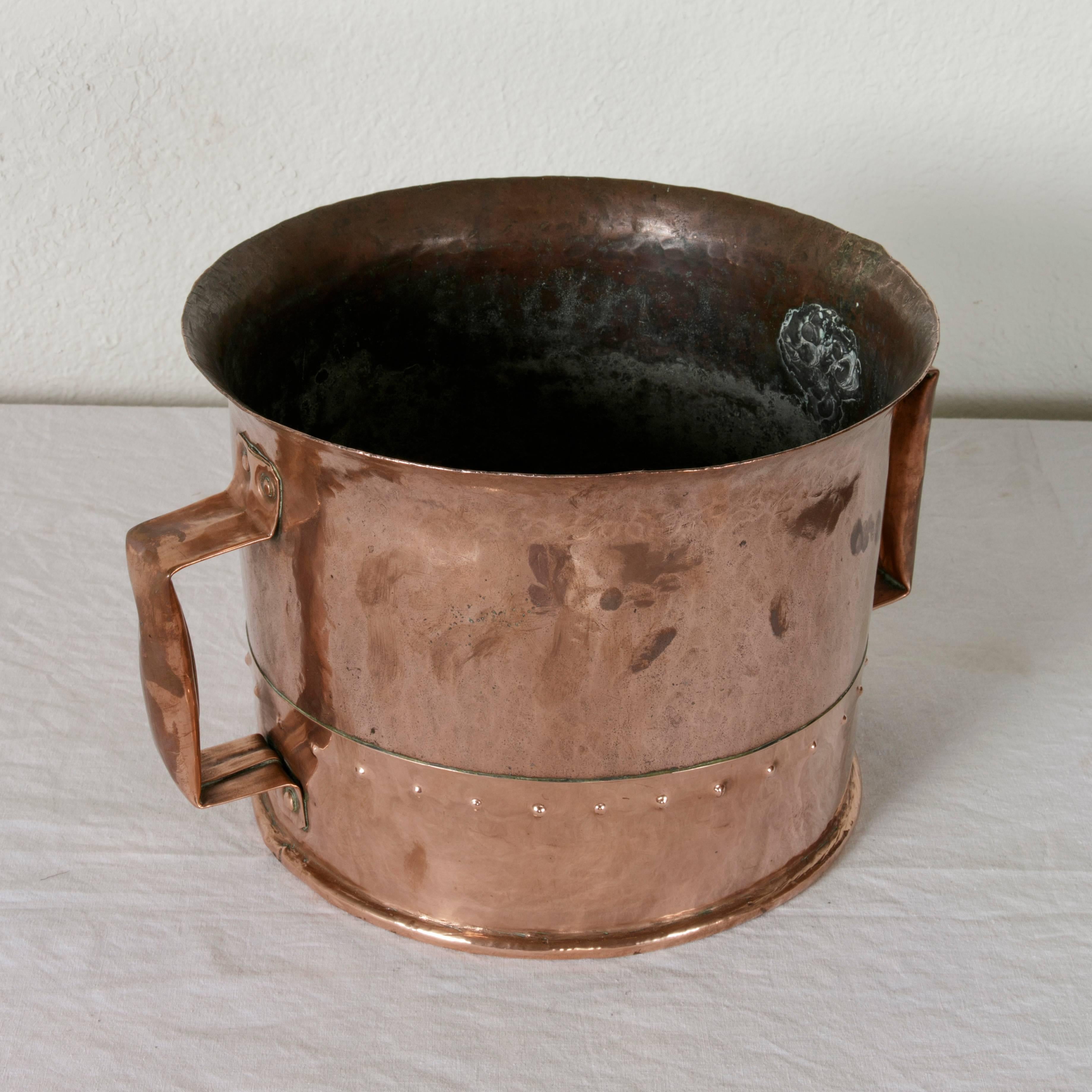 This late 19th century riveted copper water bucket features a concave bottom that was designed to help one carry the bucket on one's head to transport water. A copper riveted handle on each side allowed for the bucket to be held upright. With an
