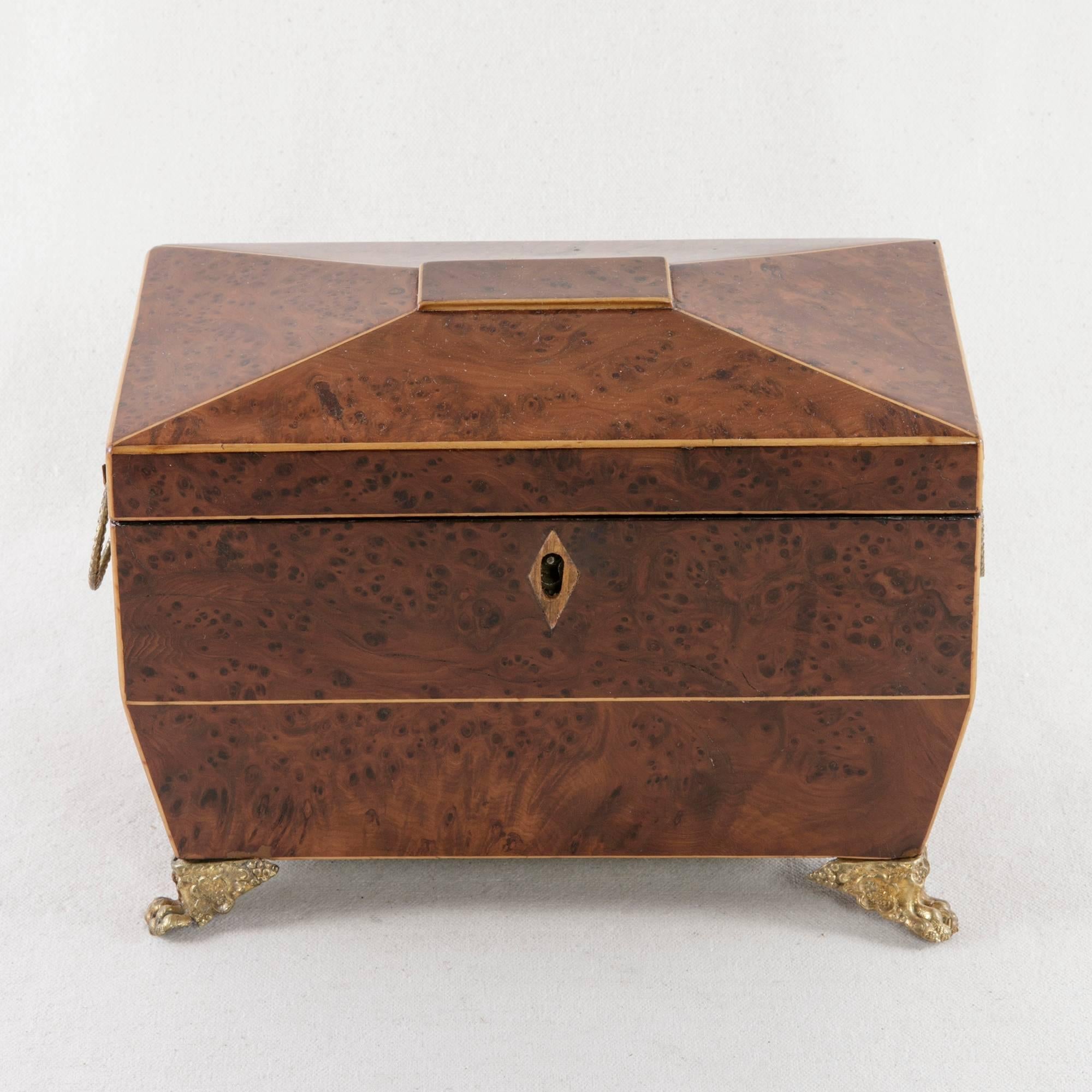 An exceptional piece from the Directoire period, this French tea caddy is constructed of burled thuya wood. Fine lines of lemon wood inlay add definition to the angled edges of the piece. Resting on bronze ormolu claw feet, this box also has bronze